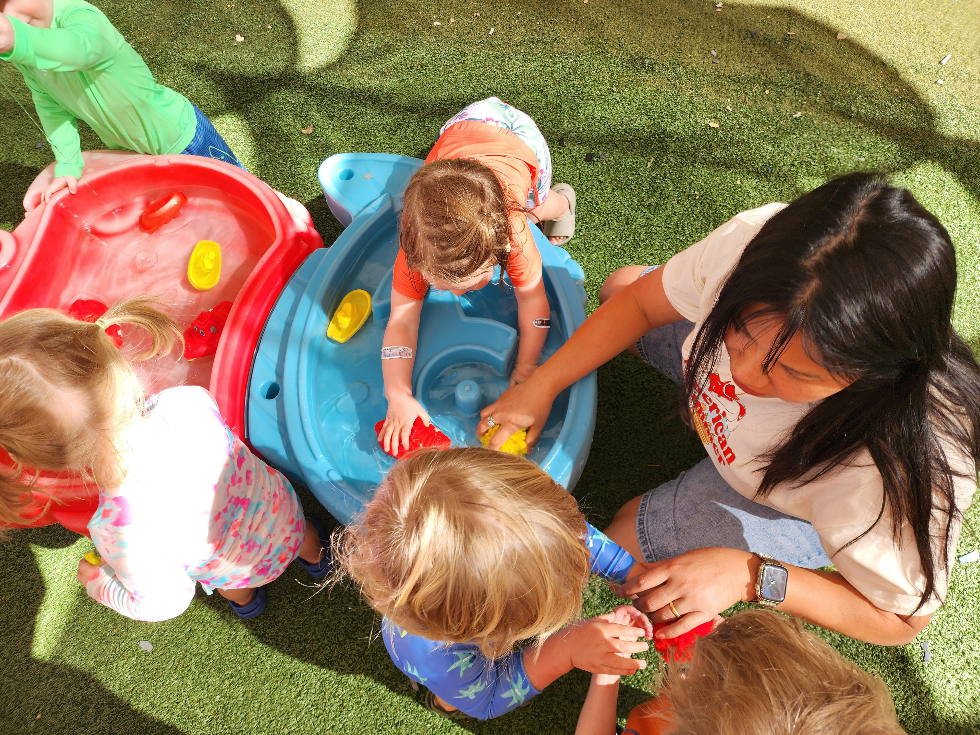 A person and children playing with water tables on artificial grass