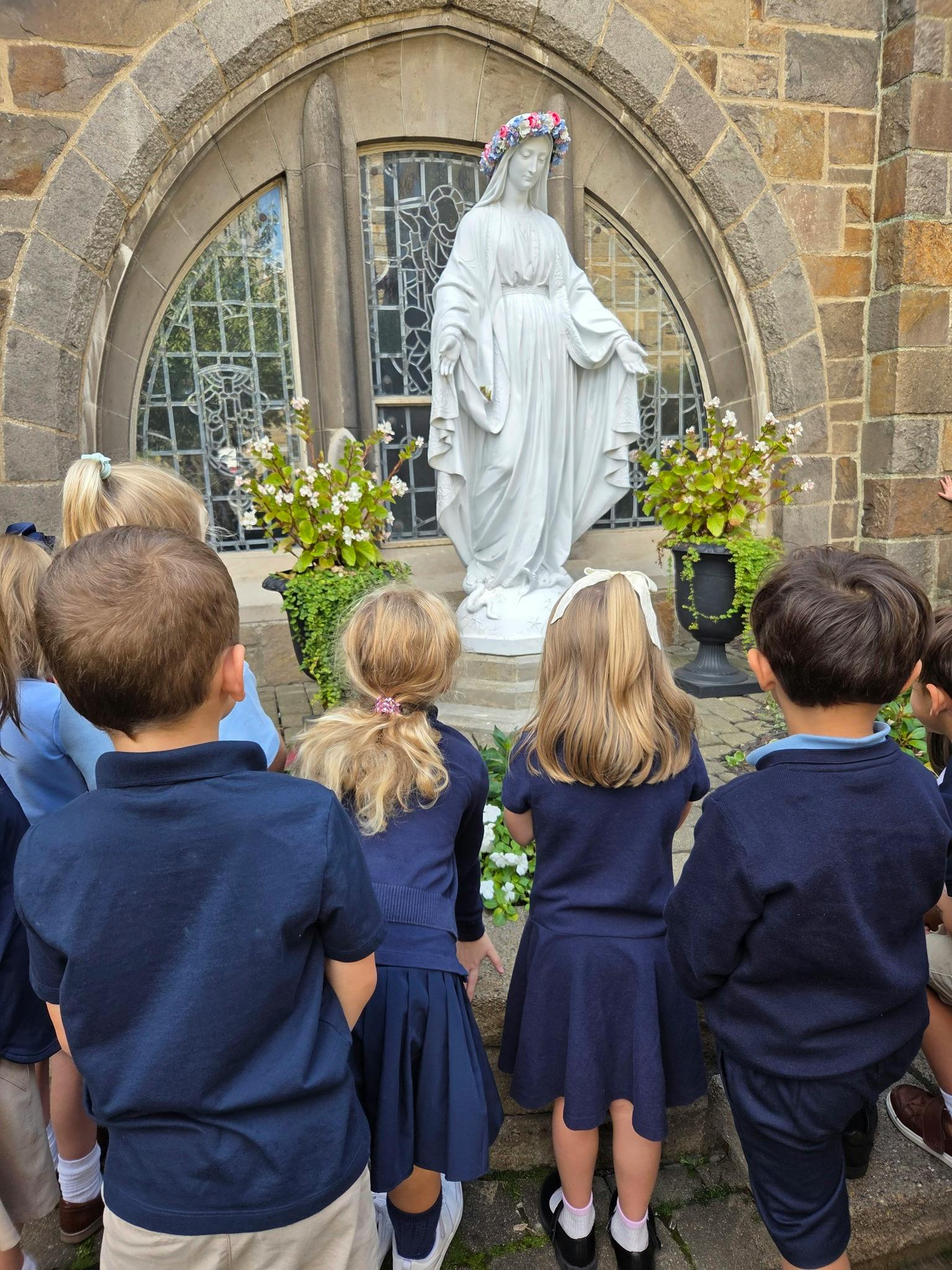 Children in uniform looking at a statue of a person with a flower crown