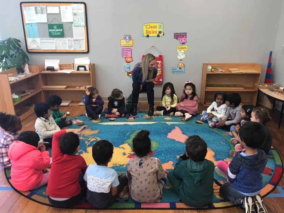 Adult and children sitting on a world map rug in a classroom