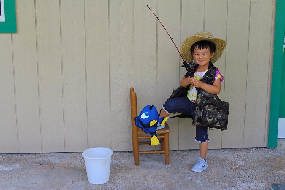 Child in a straw hat and fishing vest holding a fishing rod