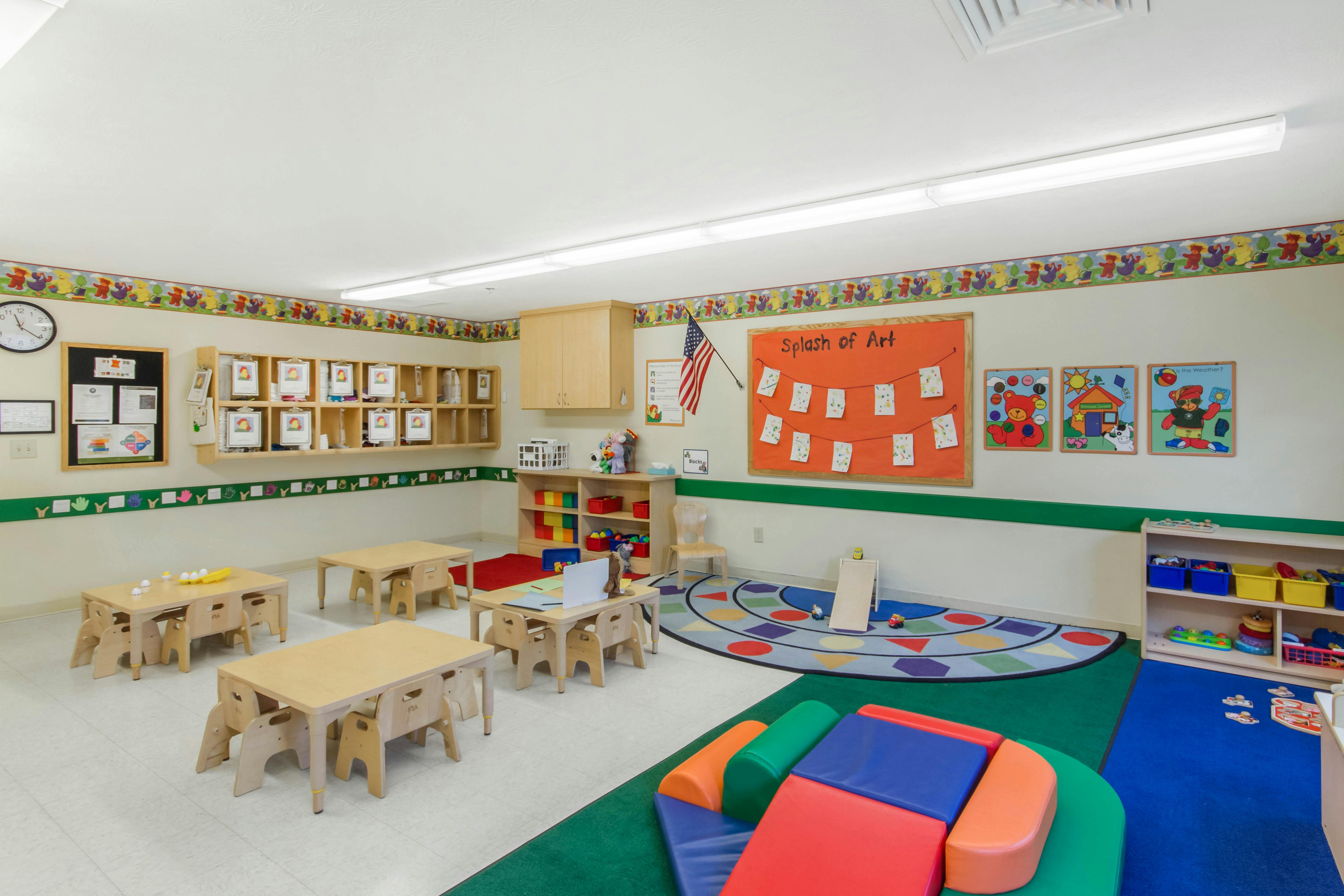 A brightly lit classroom with small tables, chairs, and play areas