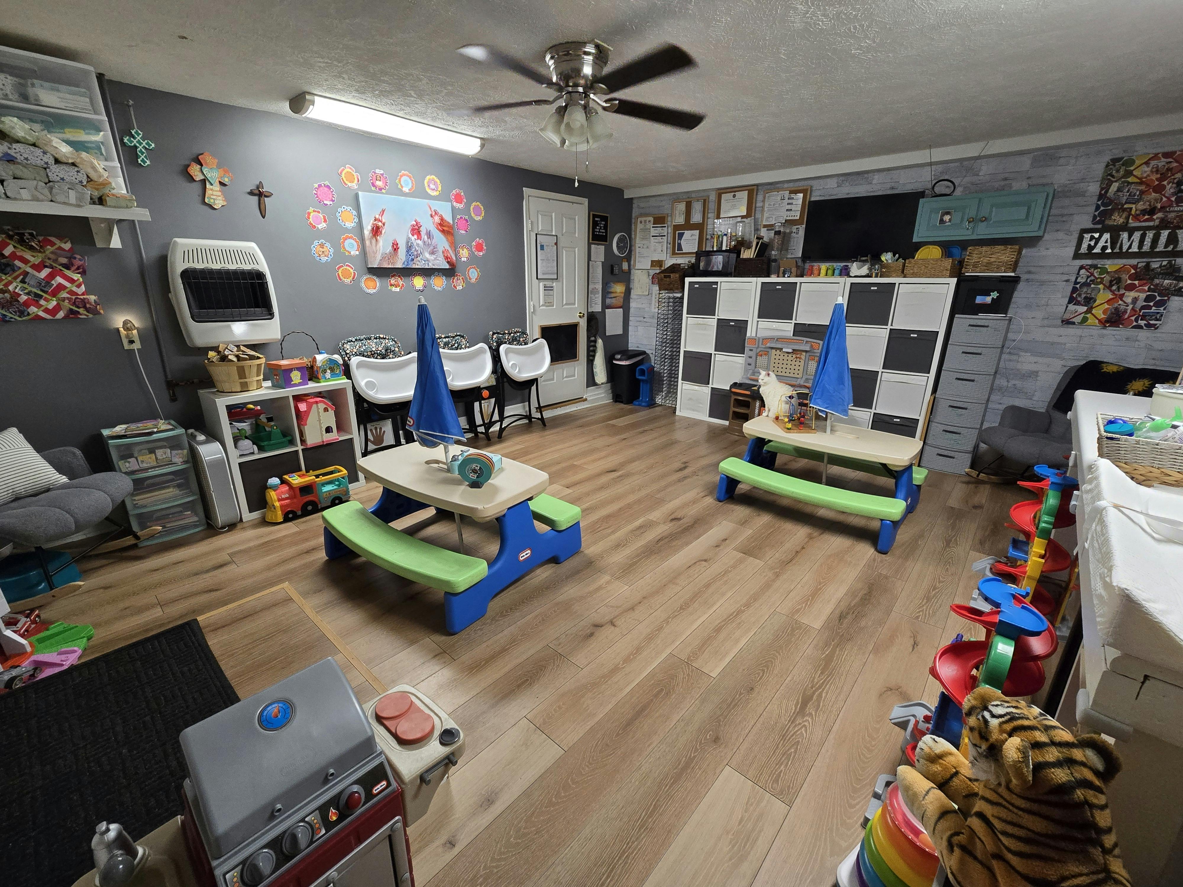 A room with child-sized picnic tables, high chairs, storage shelves, and play toys