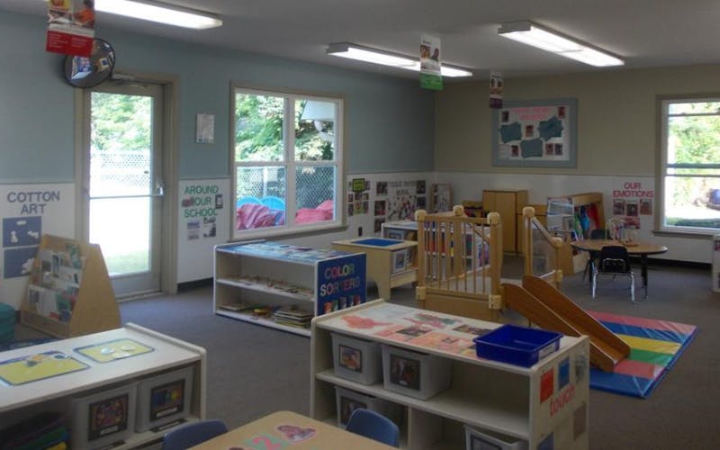 Empty classroom with small tables, shelves of toys, and a small indoor slide