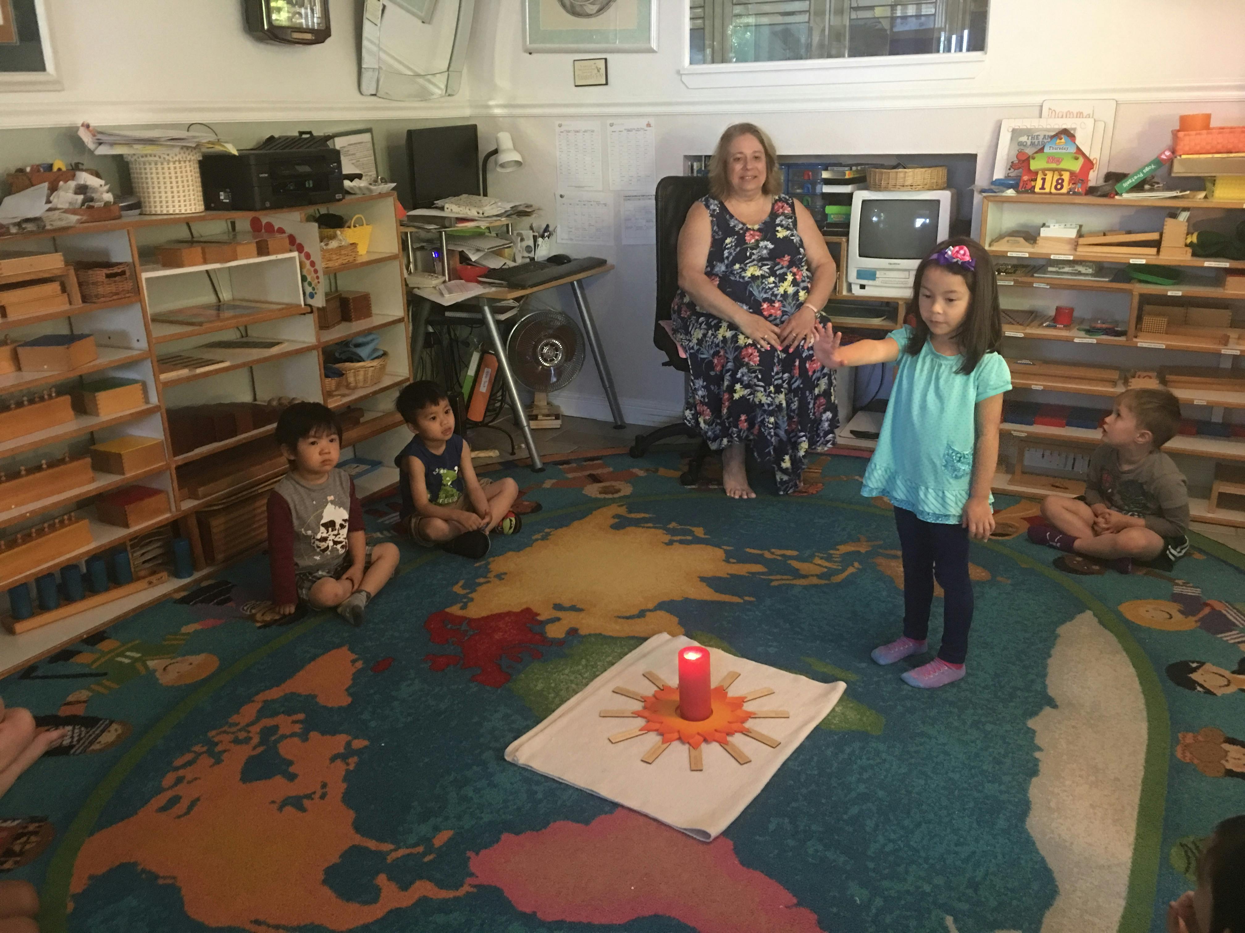 Adult and children sitting on a world map rug with a candle on a sun mat