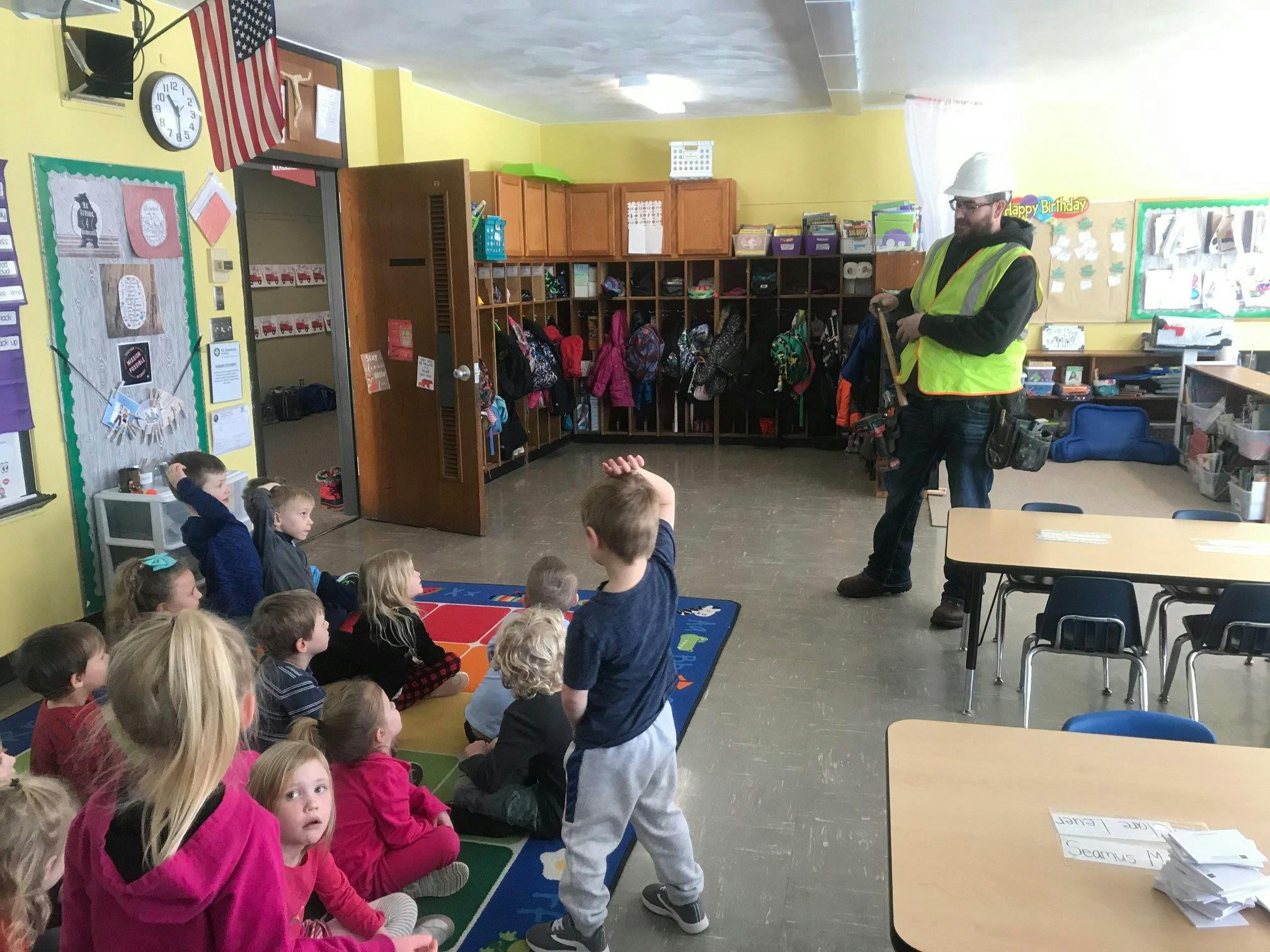 Person in hard hat and safety vest speaking to children in a classroom