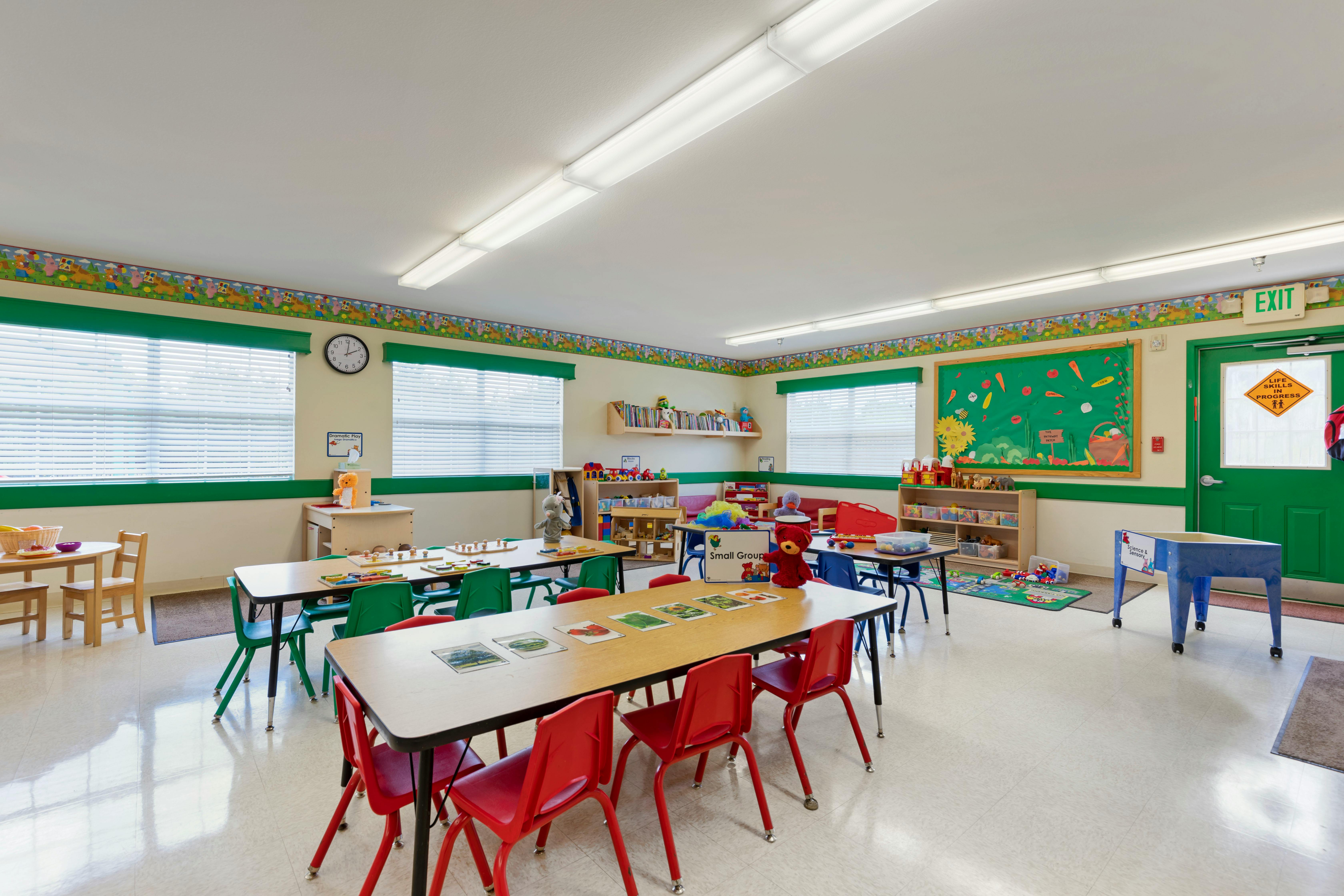 Classroom with multiple tables and chairs, toys, and educational posters on the wall