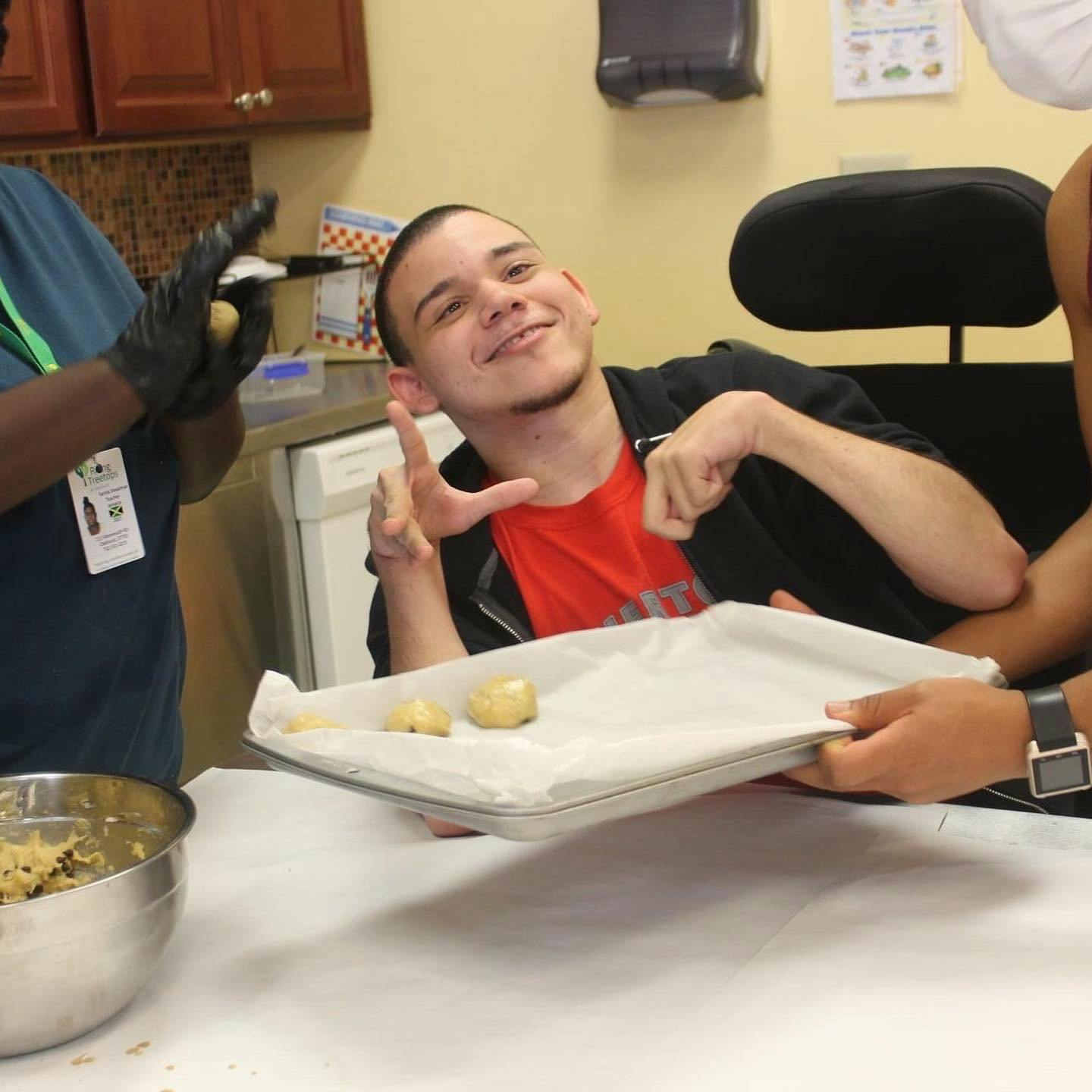 Person in black gloves placing cookie dough on a tray held baking sheet