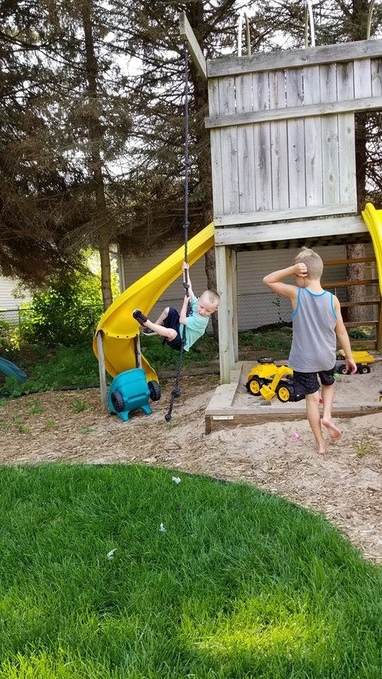 Child swinging on a rope next to a yellow slide and another child standing