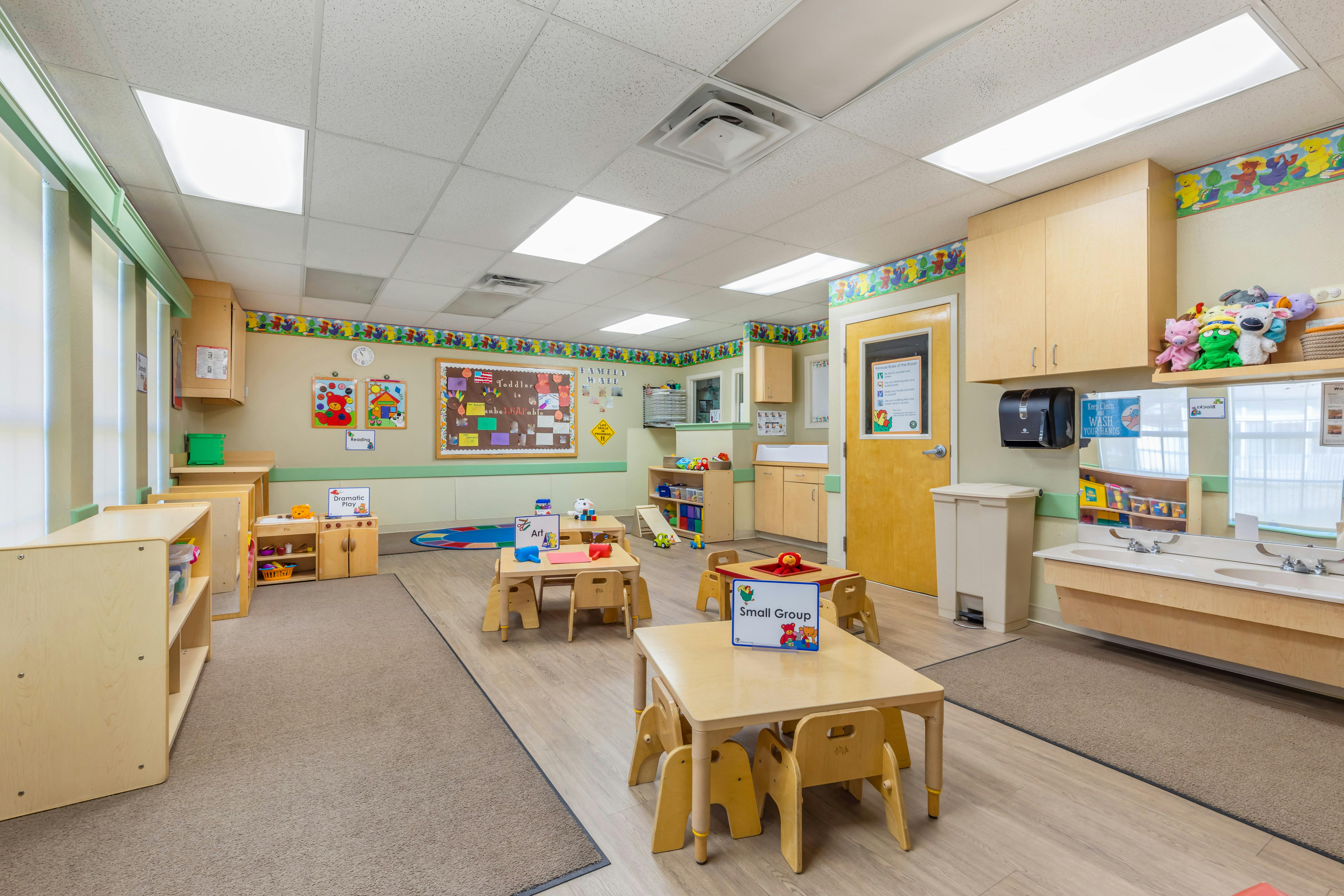 A classroom with small tables and chairs, a sink counter with mirrors, and various play areas