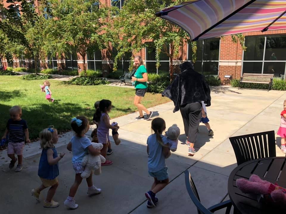 Children and adults walking outdoors, some children holding stuffed animals