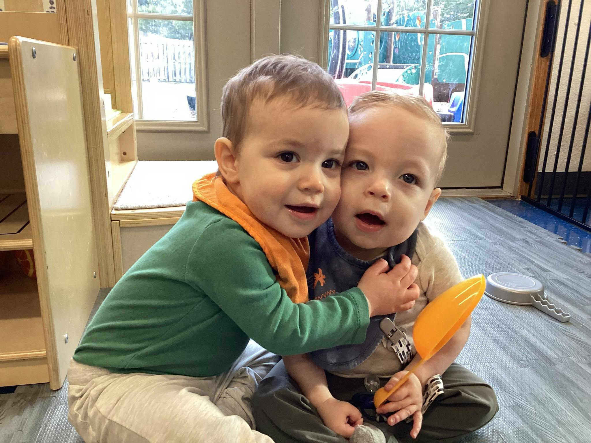 Two children sitting on the floor, one child hugging the other