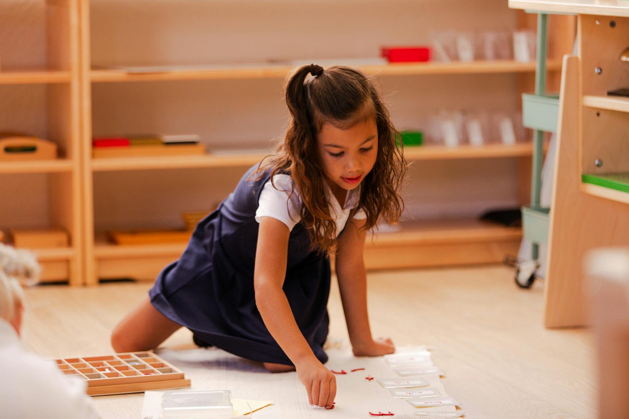 Child kneeling on floor and placing small objects on a paper
