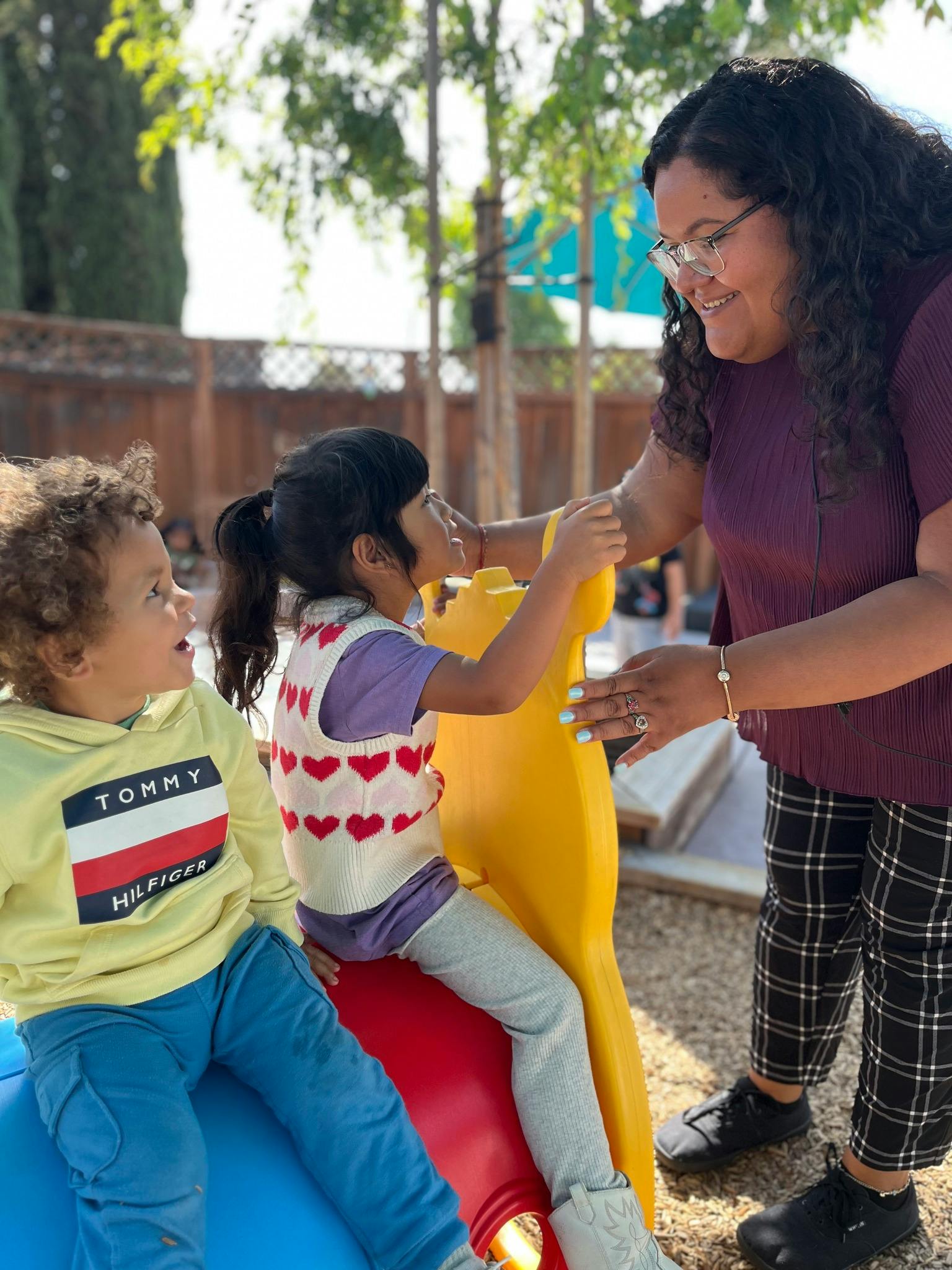 A person interacting with two children playing on playground equipment