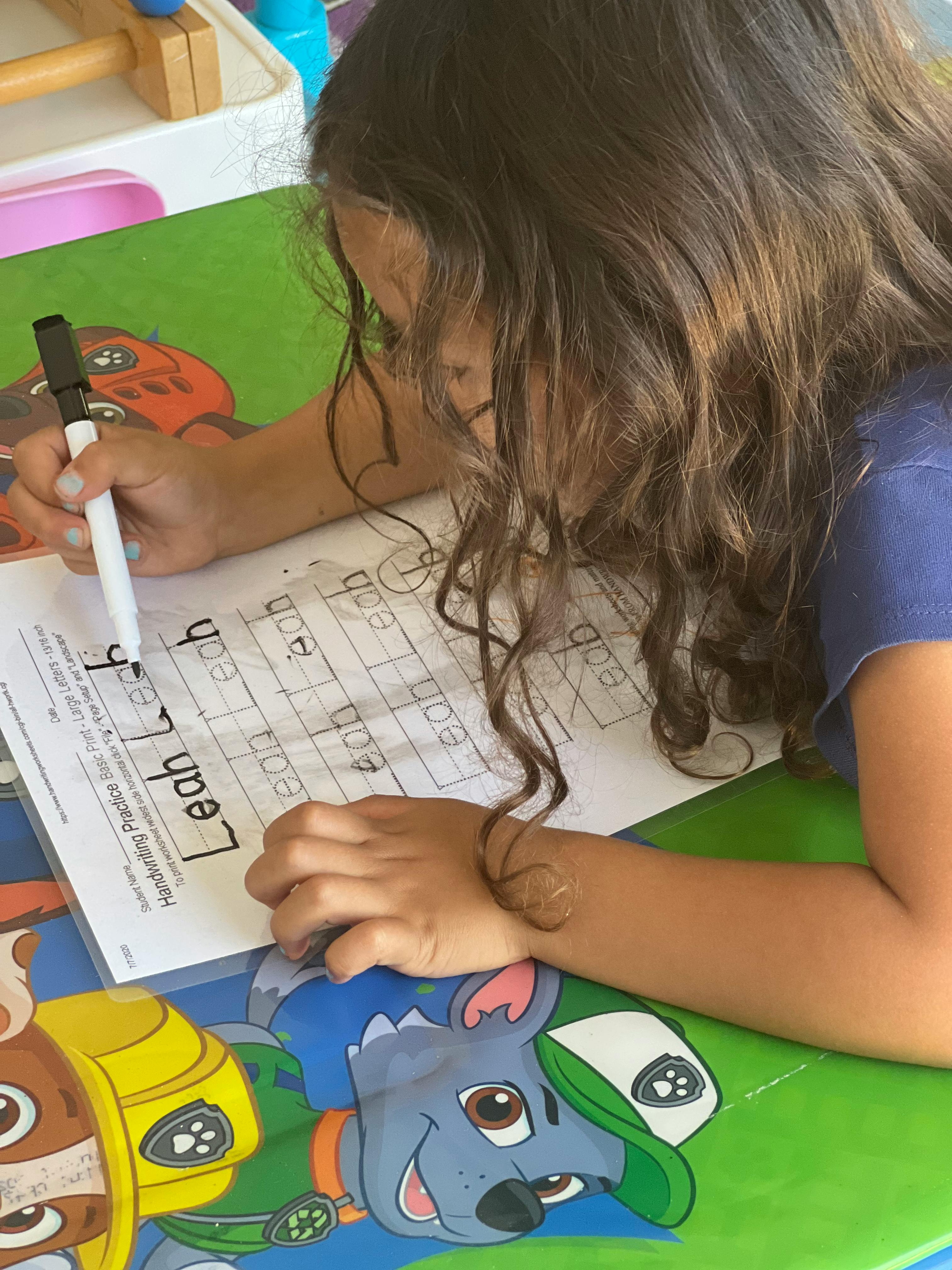 Child writing on a worksheet with a marker