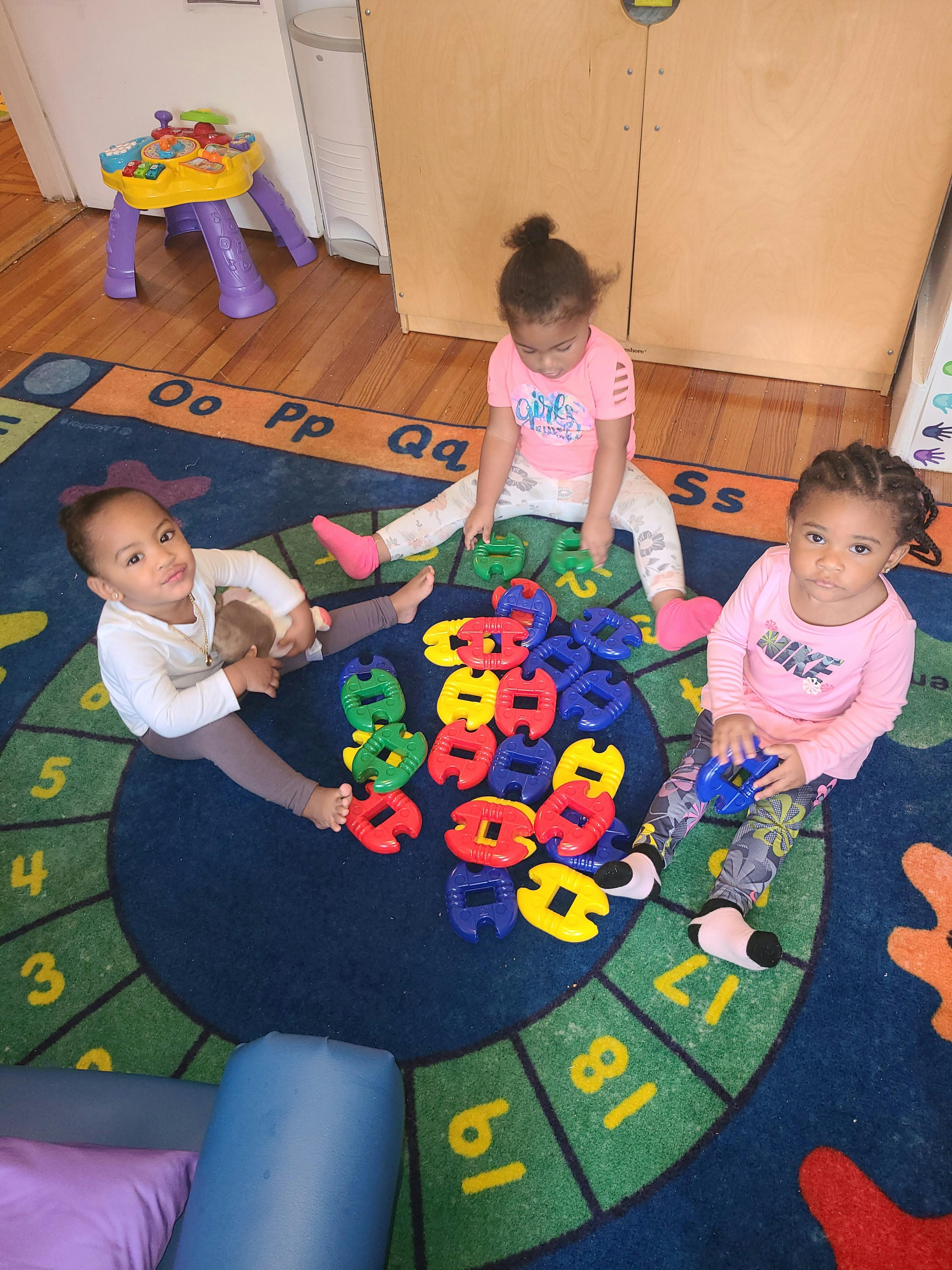 Three children playing with colorful interlocking toys on a rug