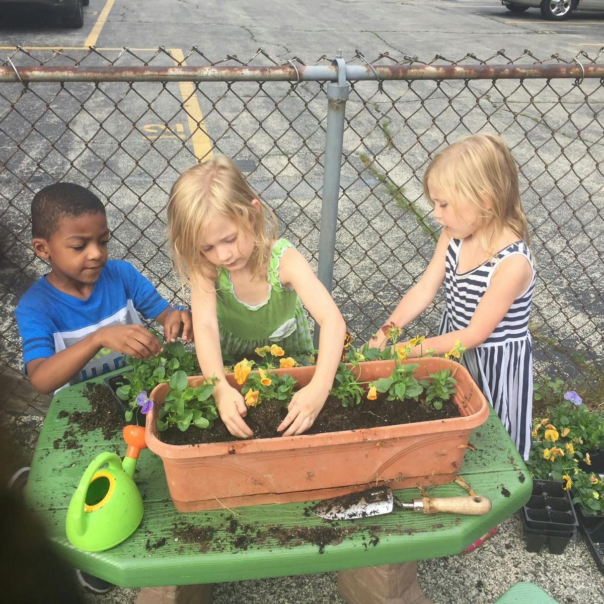 Three children planting flowers in a planter