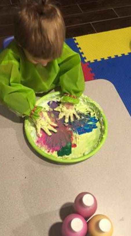 Child in a green smock finger painting in a tray