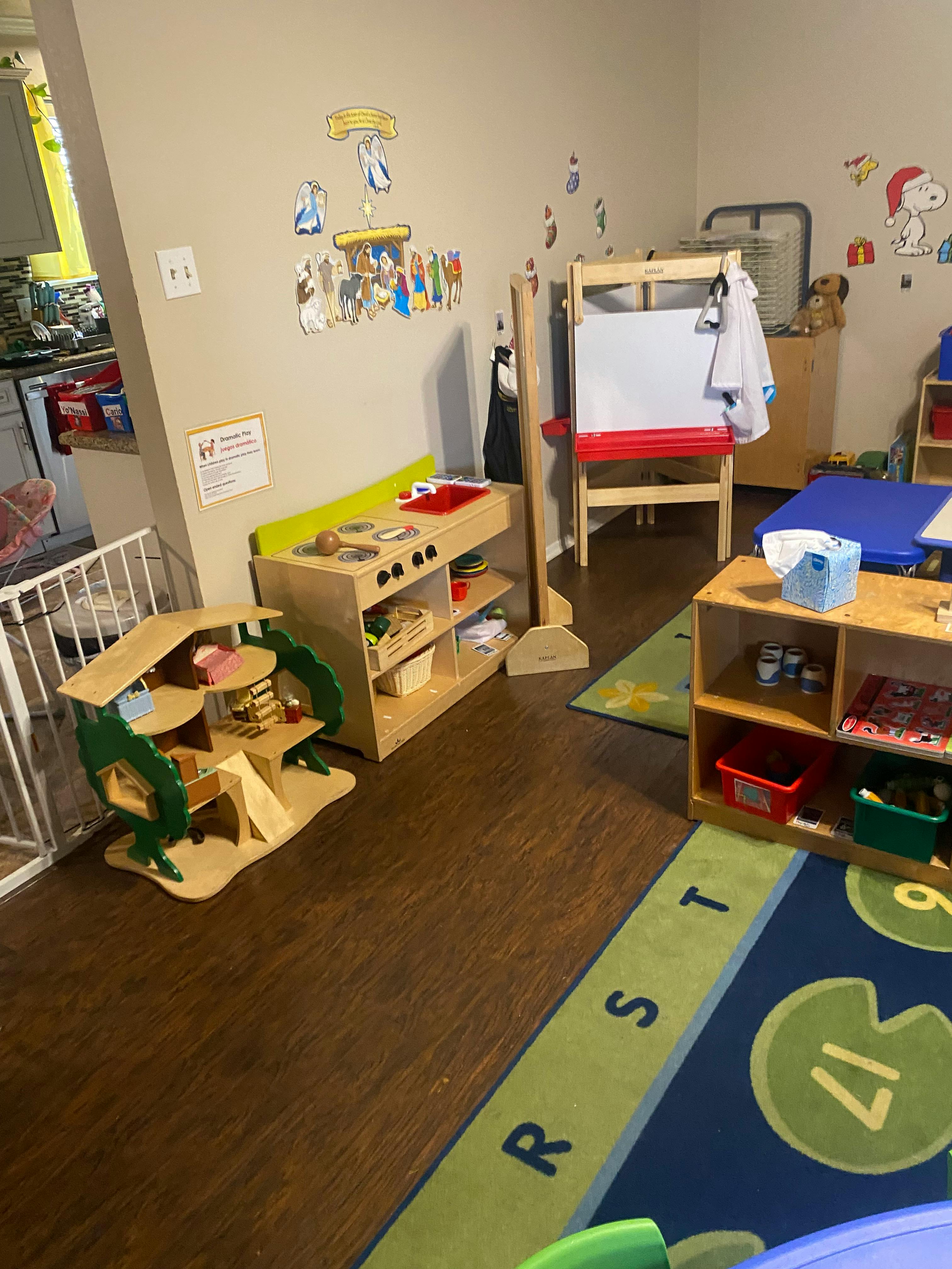 Playroom with wooden play kitchen, dollhouse, easel, and alphabet rug