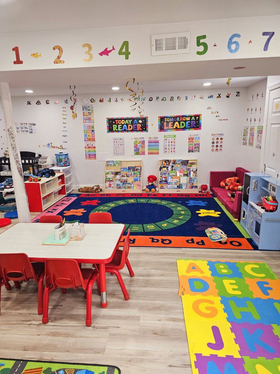 Classroom with small tables and chairs, colorful rugs, and educational posters