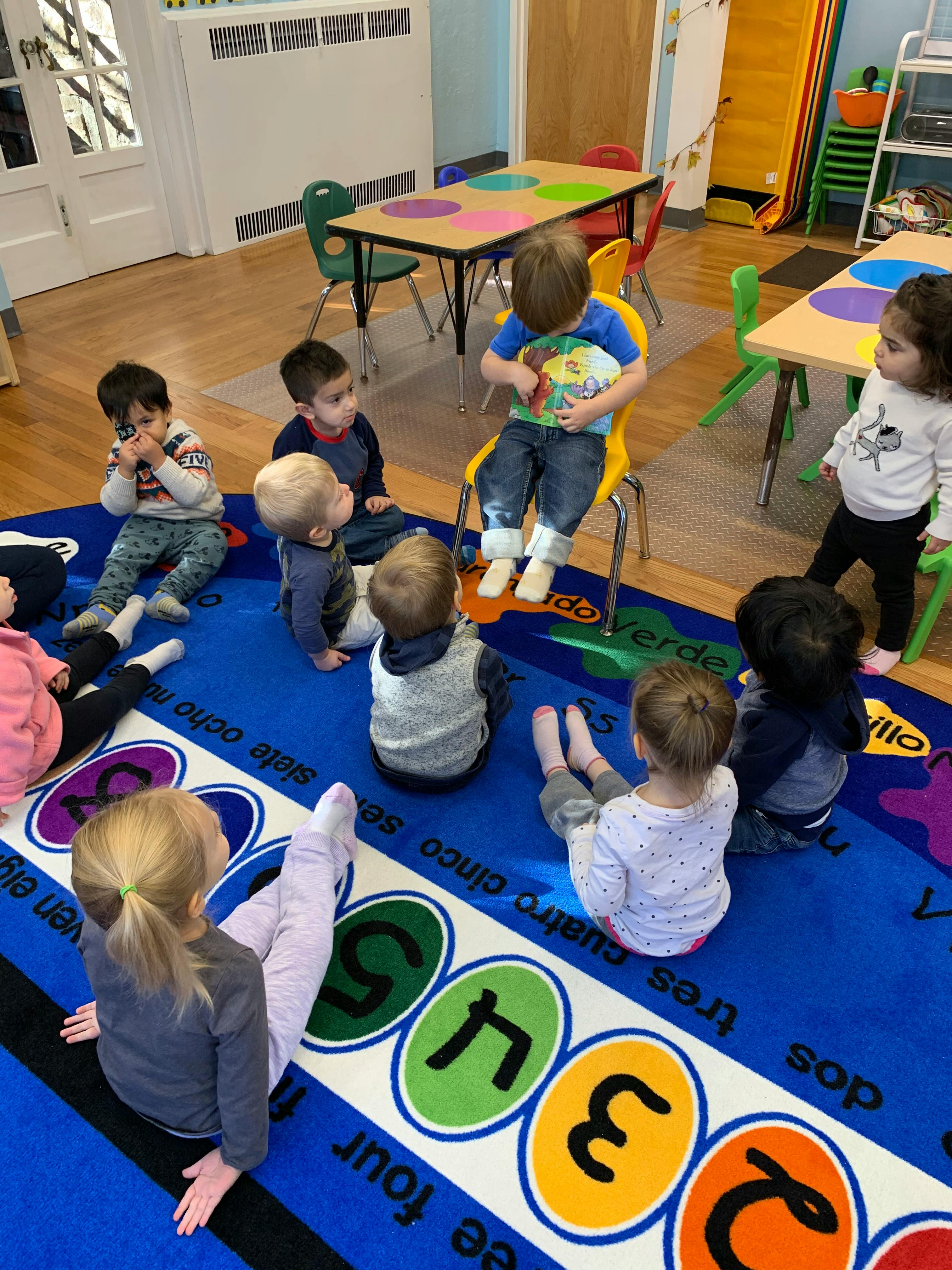 Children sitting on a blue rug with numbers and words