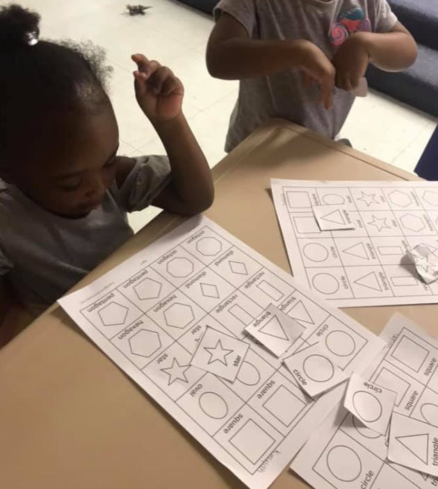 Child looking at a paper with shapes, another child in the background