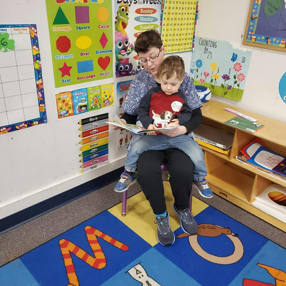 Person reading a book to a child sitting on their lap in a classroom
