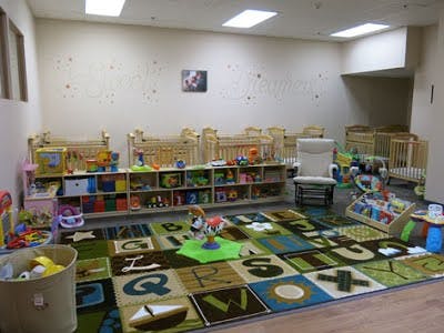 Nursery room with cribs, shelves of toys, and an alphabet rug