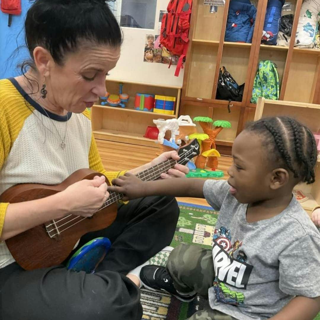 Person playing ukulele with a child in a classroom