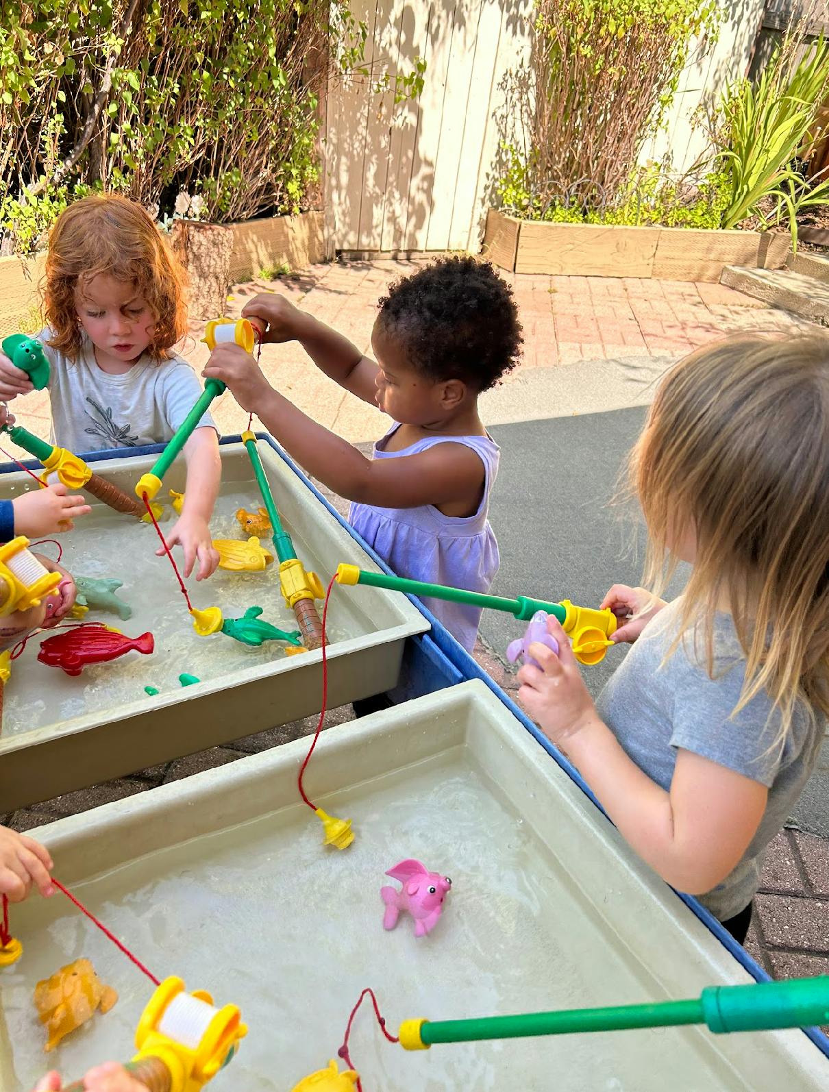 Children playing with toy fishing rods in water tables