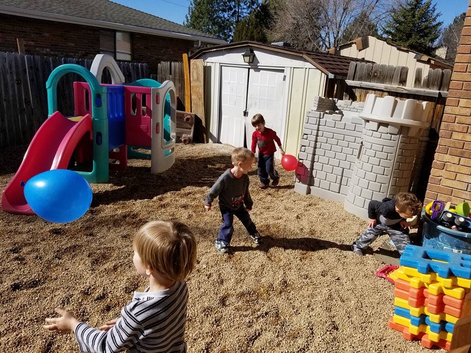 Children playing in a sandy backyard with a slide and play structure