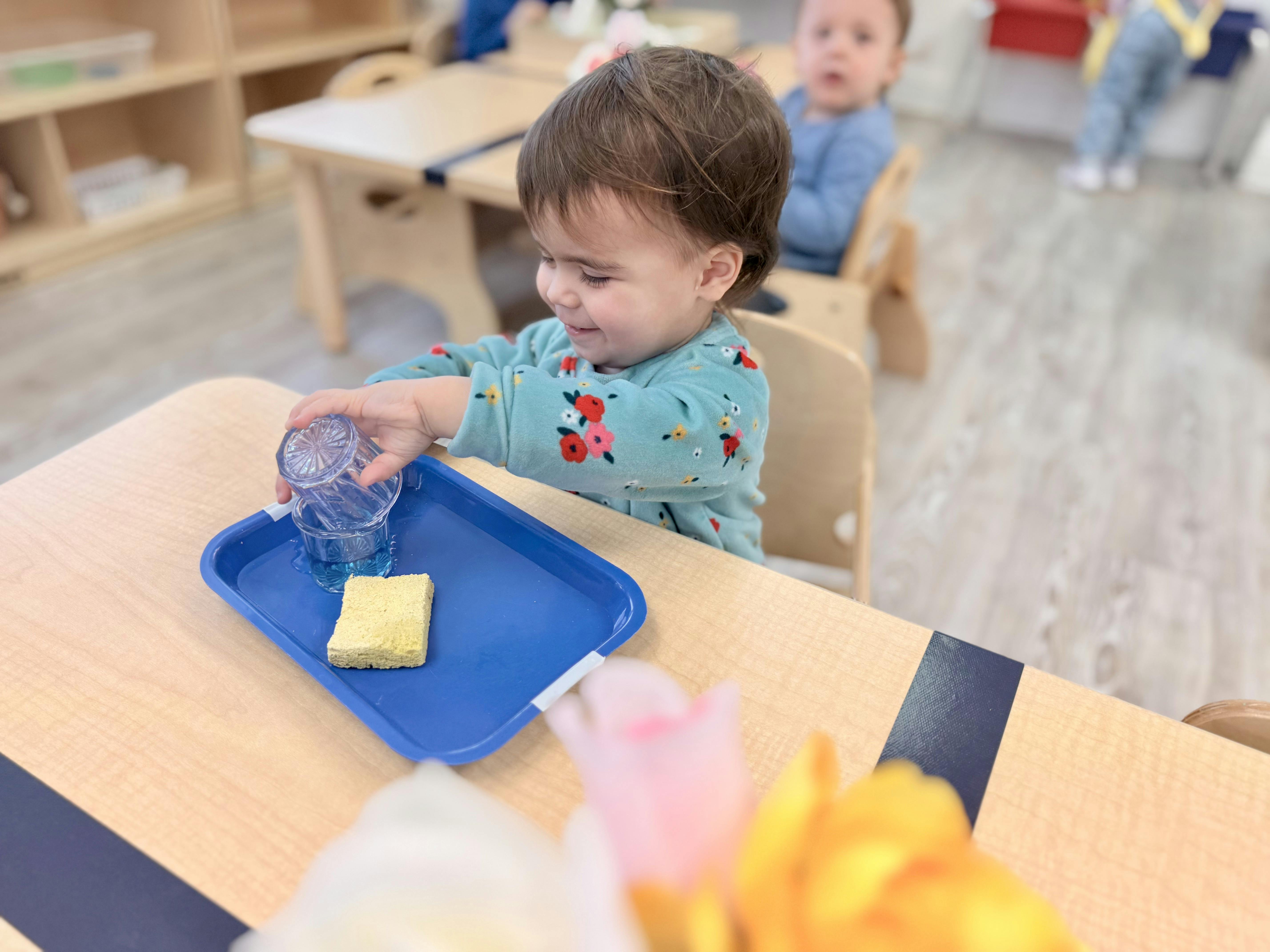 Child pouring from one glass to another on a tray with a sponge
