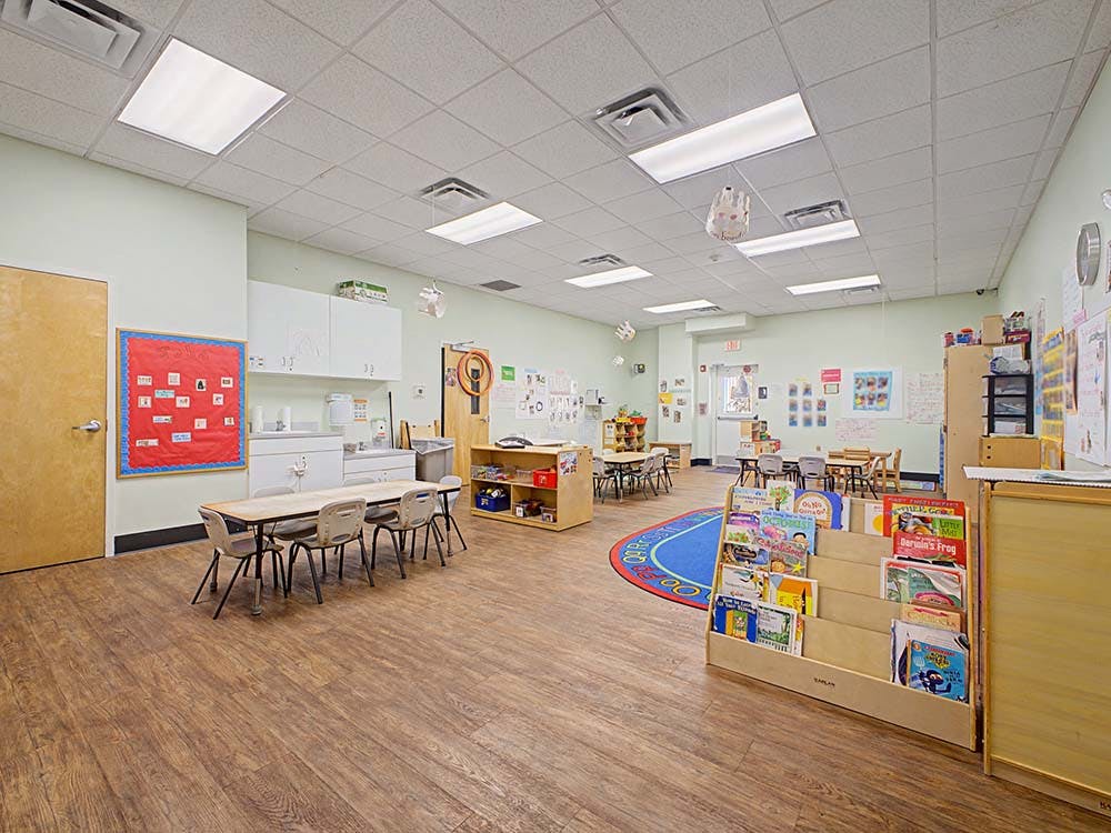 An empty early childhood classroom with small tables and chairs