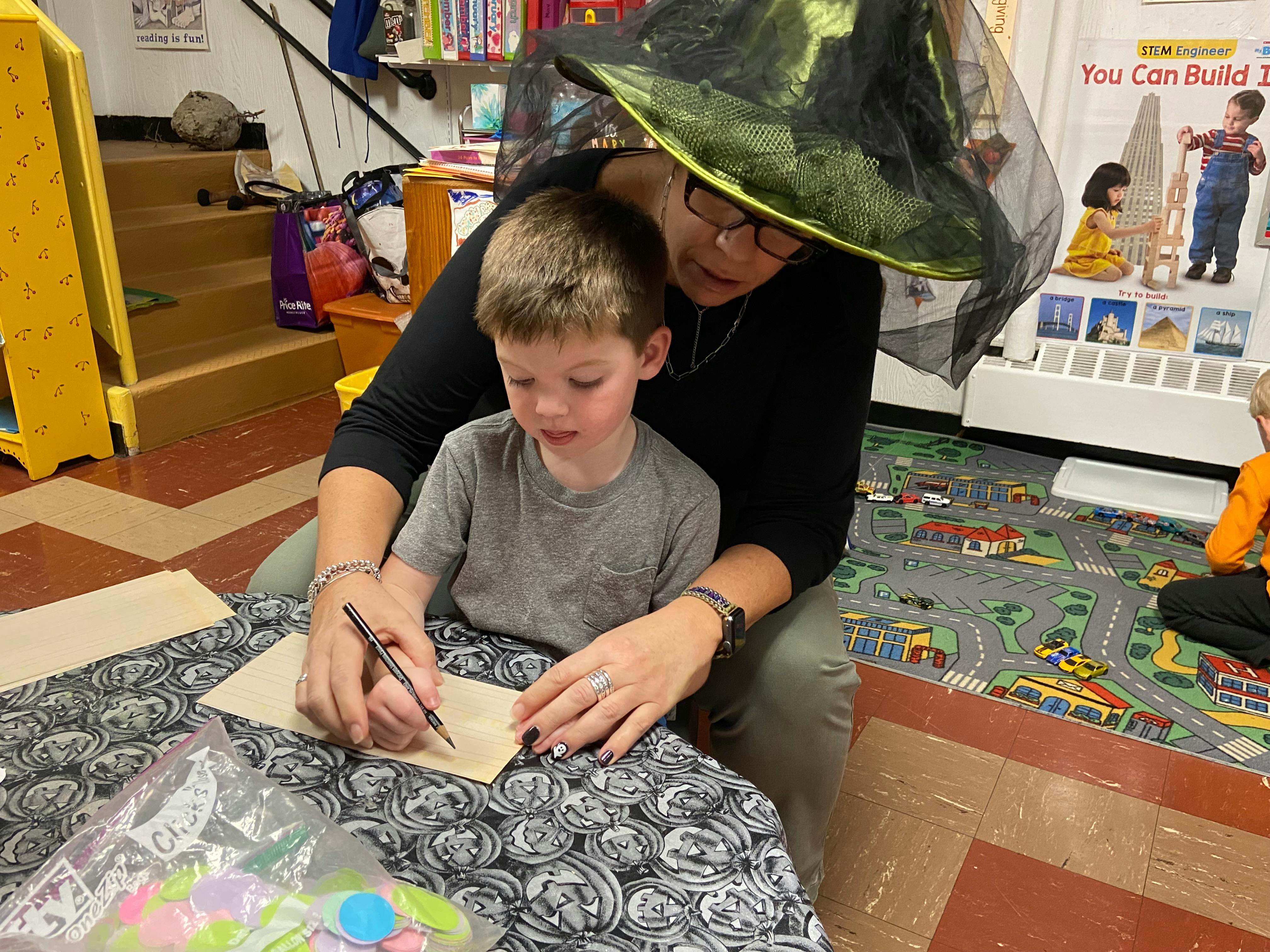 Person in witch hat helping child write on paper