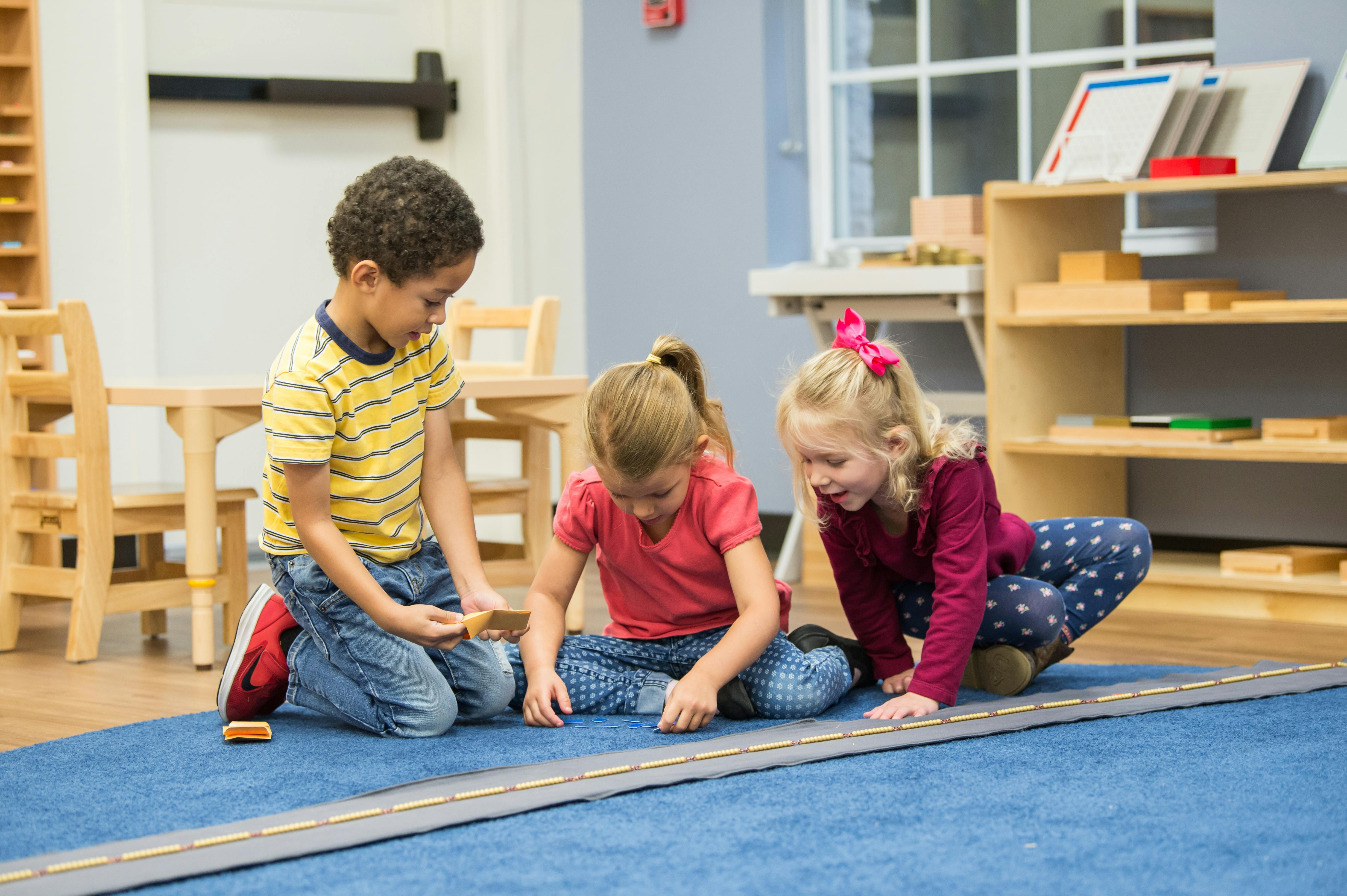 Three children playing with blocks on a blue rug in a classroom