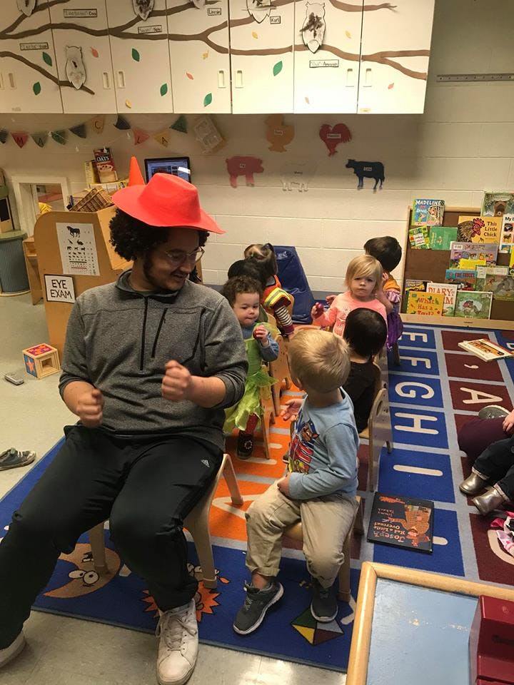 Person in red hat sitting with children in a classroom