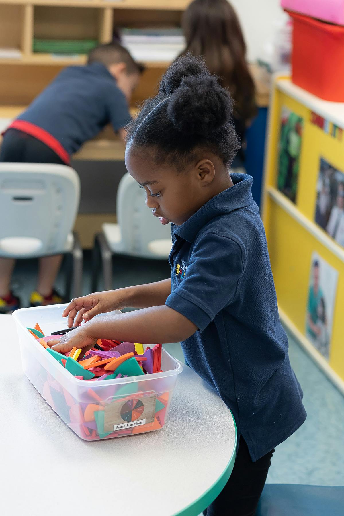 Child reaching into a clear bin of colorful shapes in a classroom