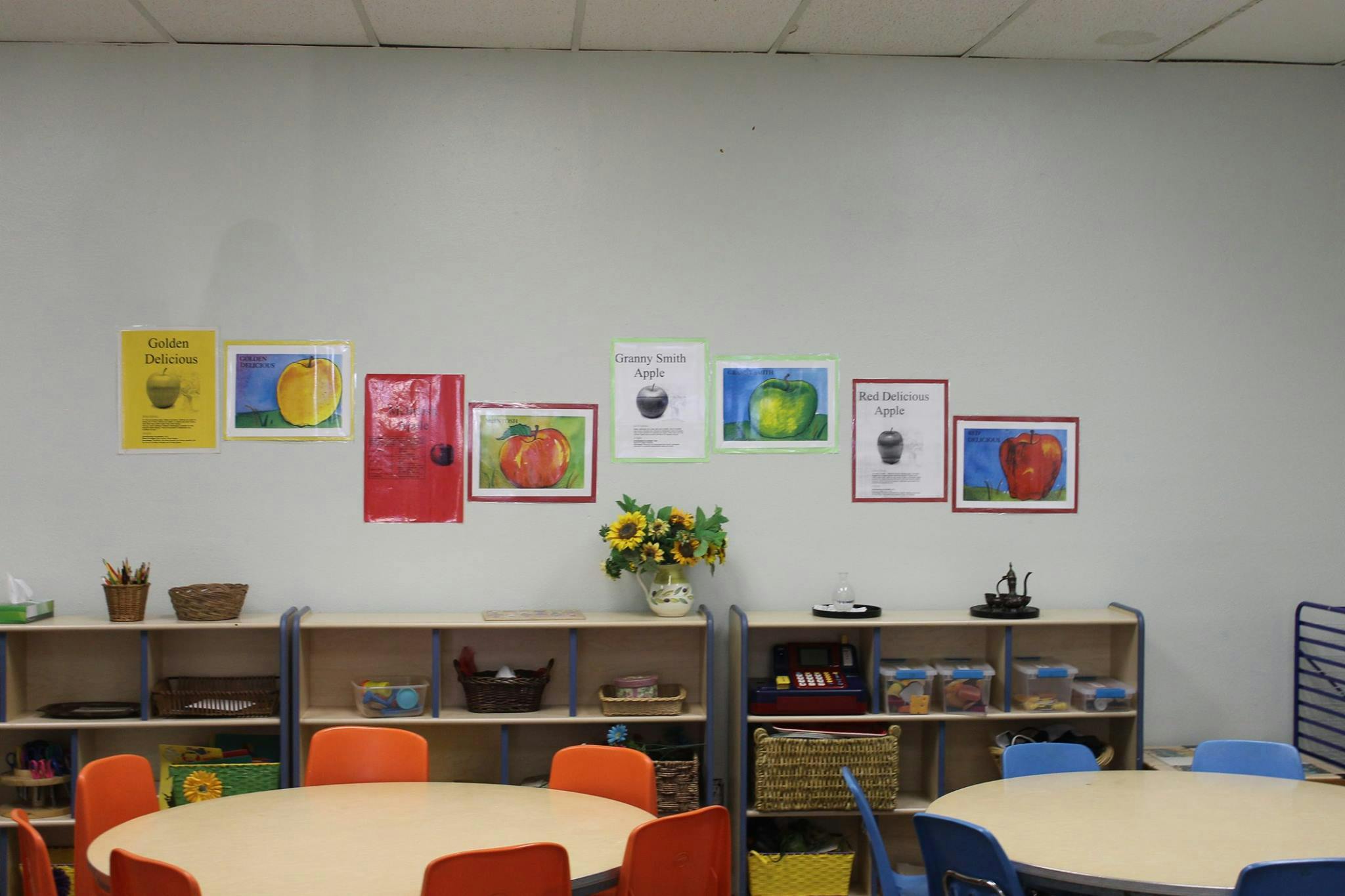 Classroom with tables, chairs, shelves, and fruit-themed artwork on the wall