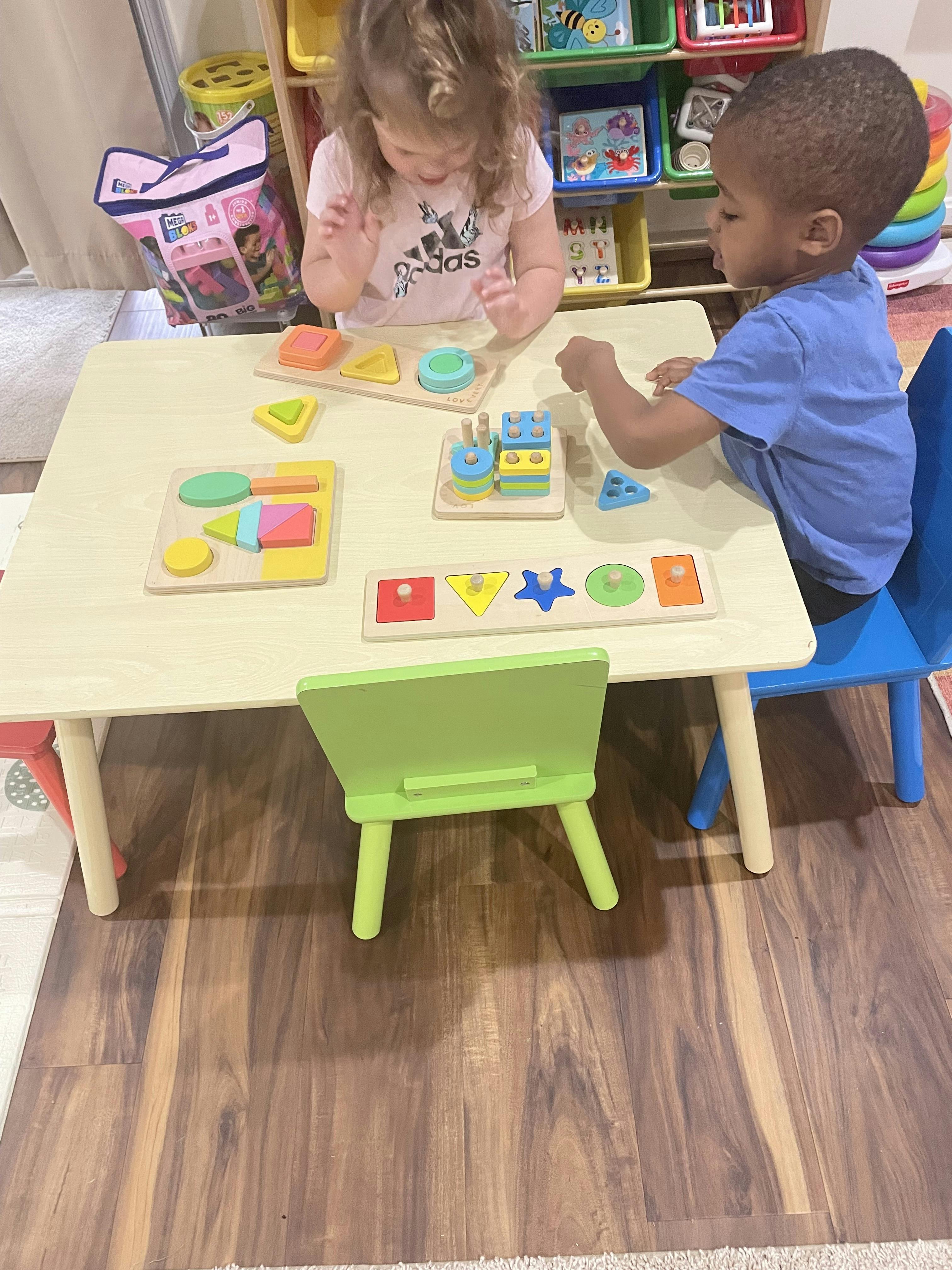 Two children playing with shape puzzles at a small table