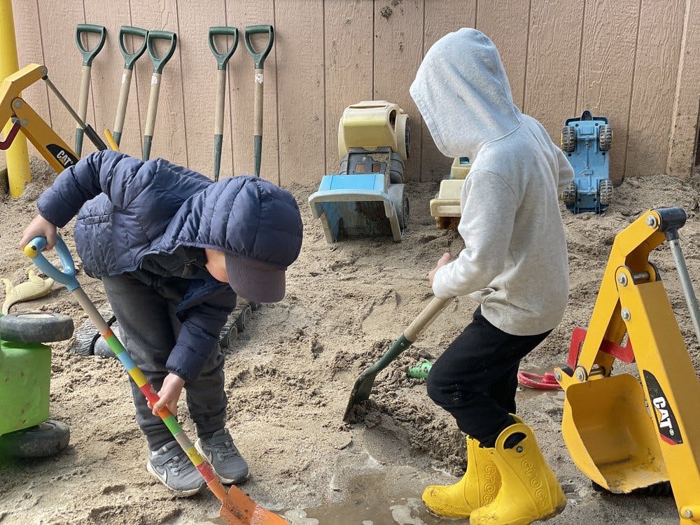 Two children digging in sand with shovels