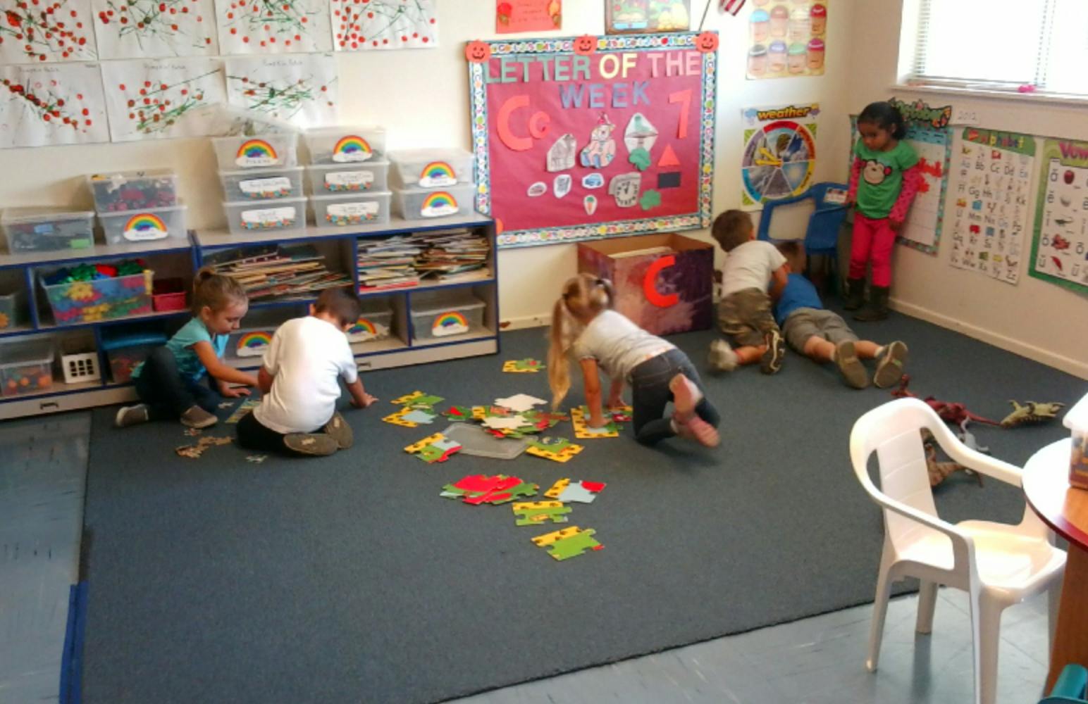 Children playing with puzzles on the floor in a classroom