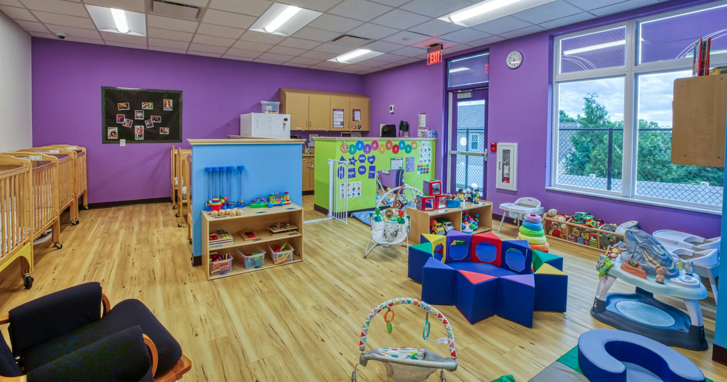 A childcare classroom with purple walls, cribs, toys, and activity centers