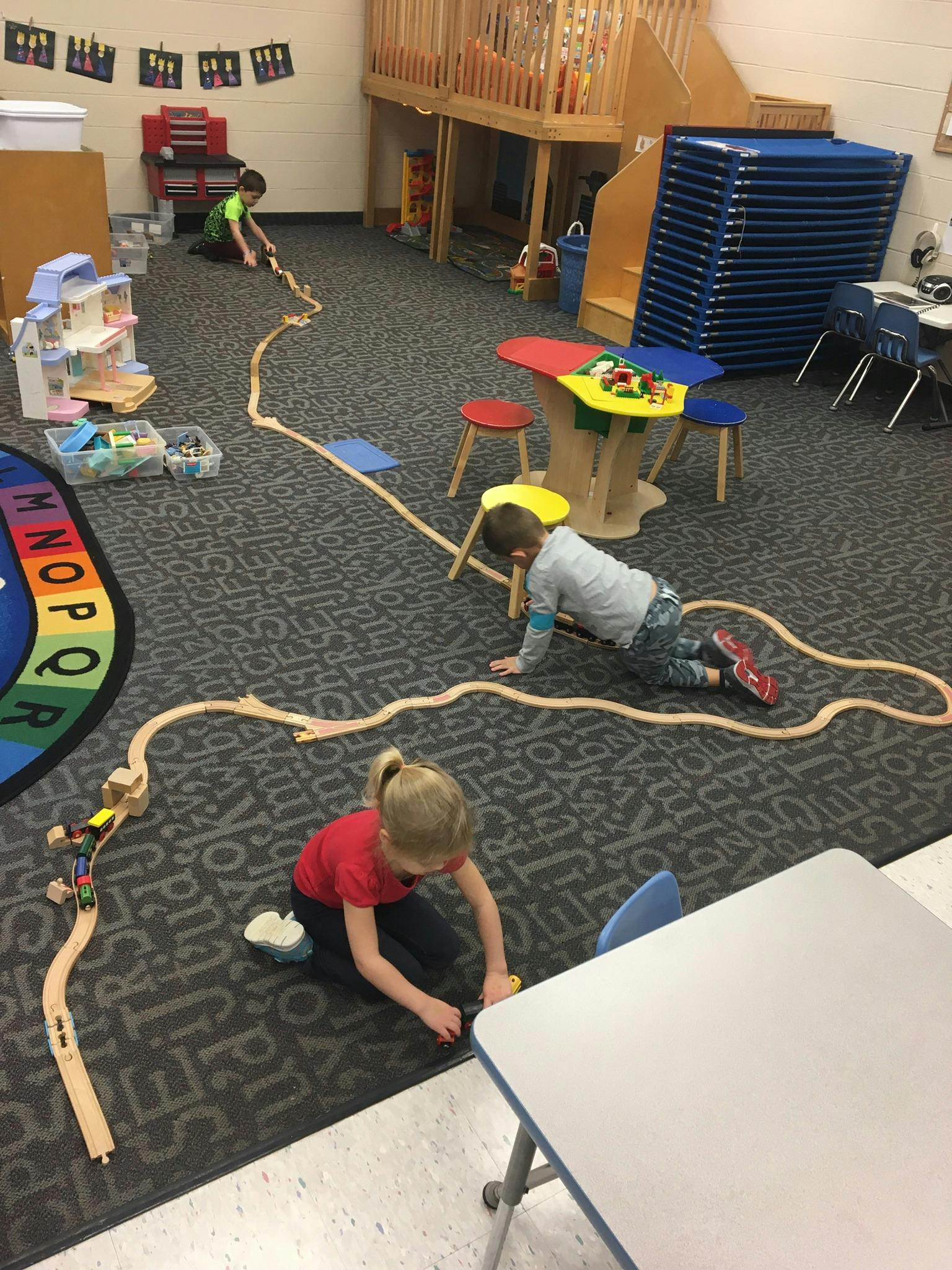 Children playing with a wooden train set on the floor of a classroom