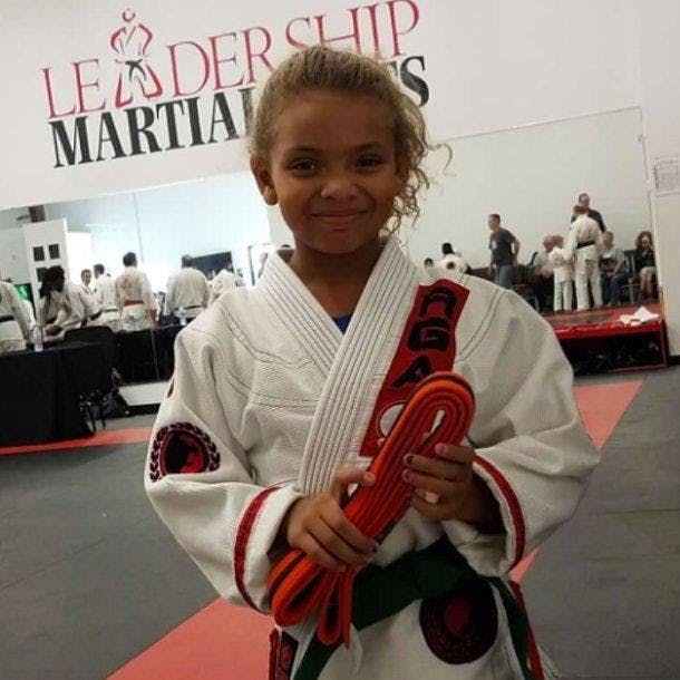 Child in martial arts gi holding a red and orange belt