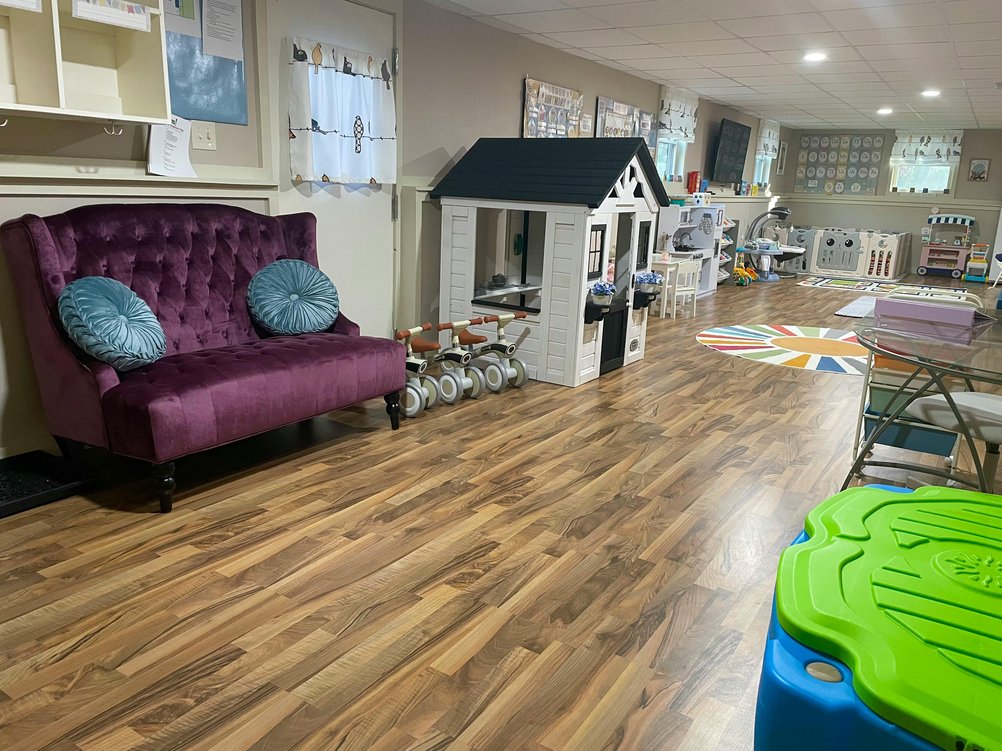Purple sofa, playhouse, and tricycles in a room with wood flooring