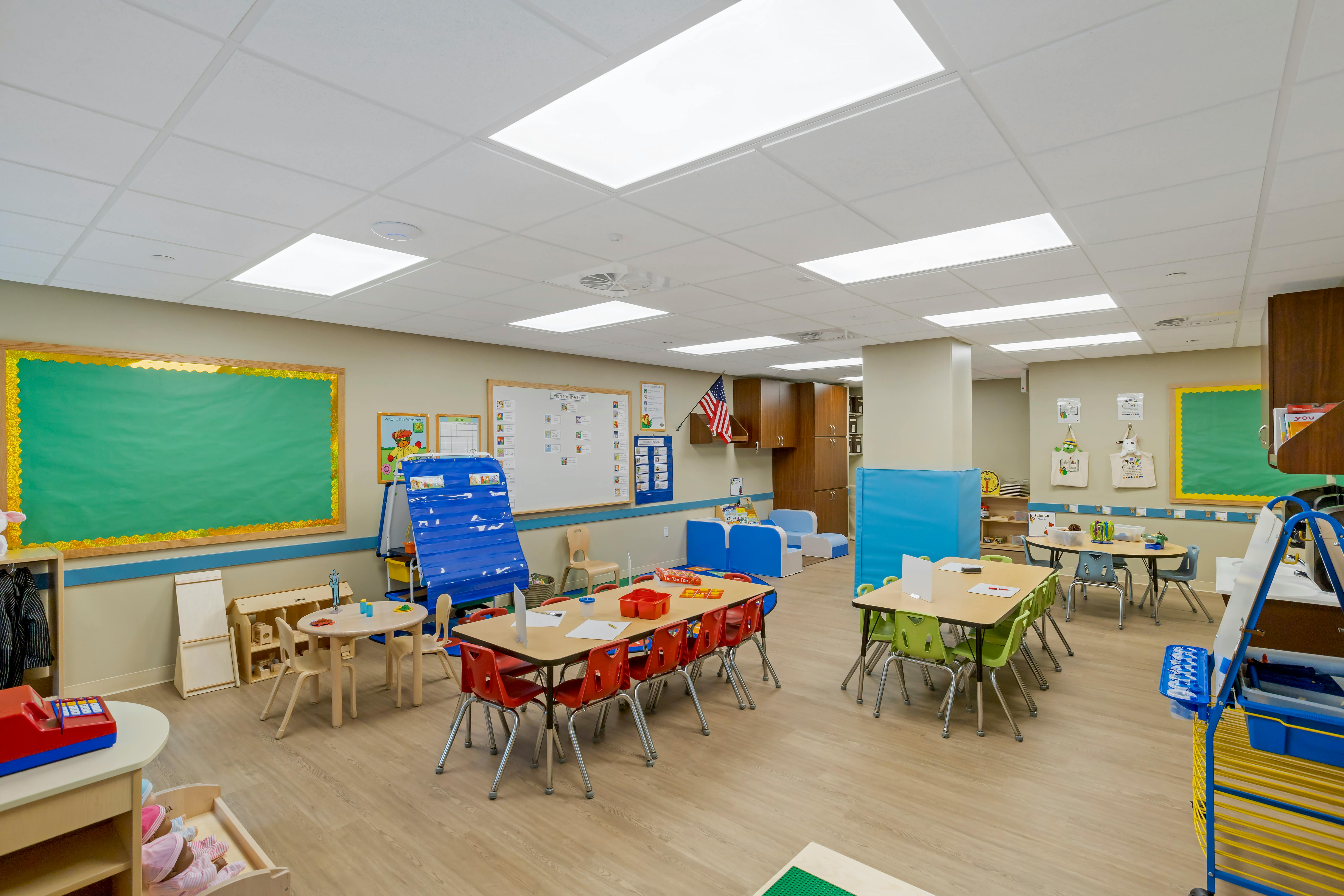 Colorful classroom with child-sized tables and chairs, play area, and whiteboards