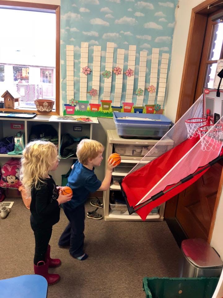 Two children playing with basketballs in a classroom