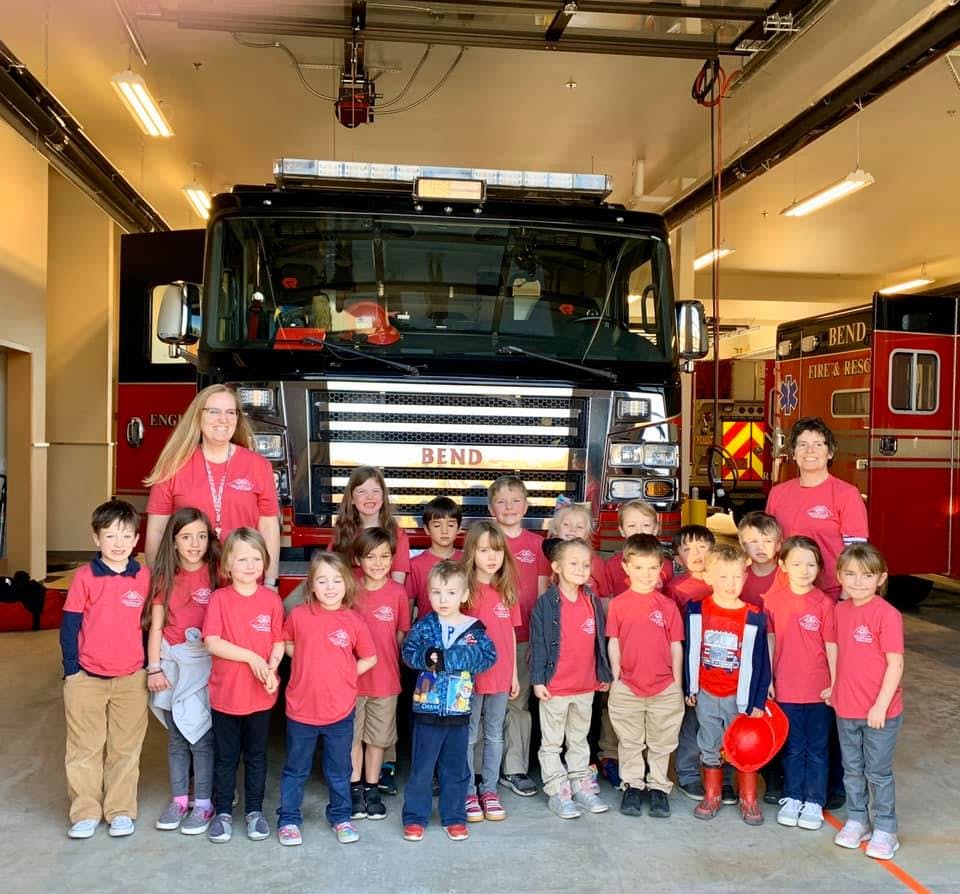 Two adults and many children in red shirts standing in front of a fire truck