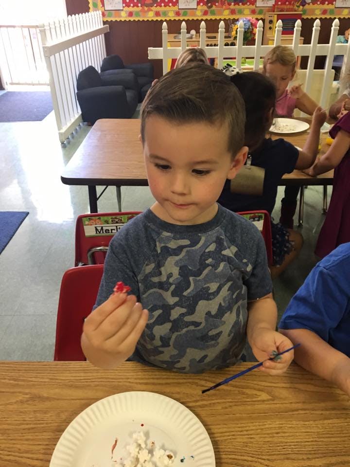Child holding a small red object in a classroom