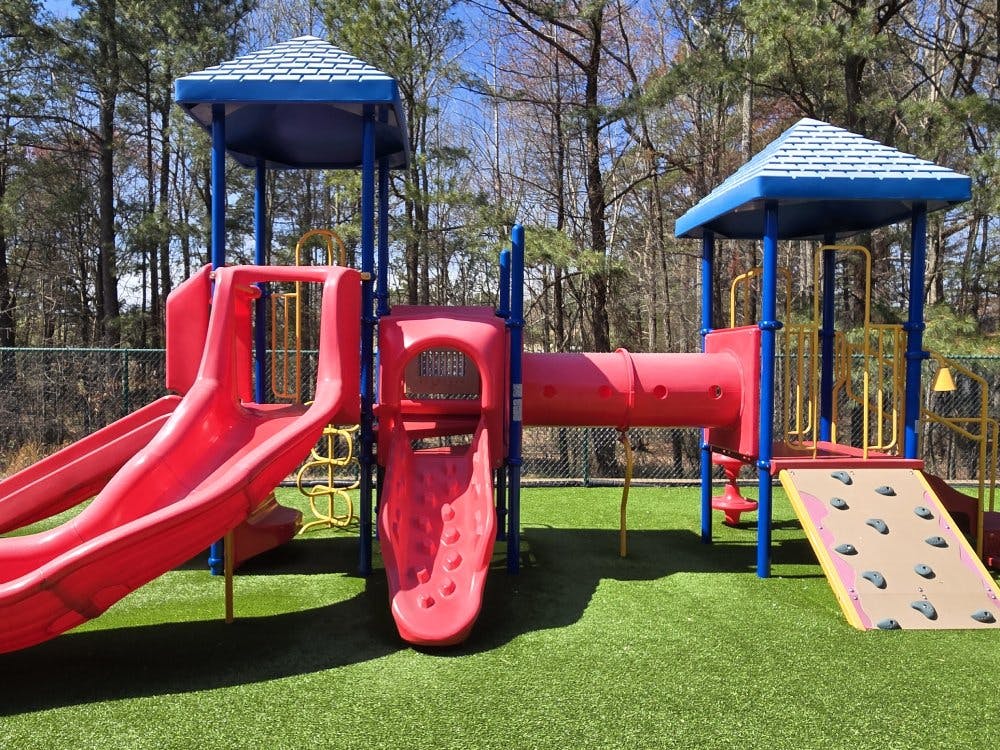 Red and blue playground with slides, tunnels, and climbing wall on green turf