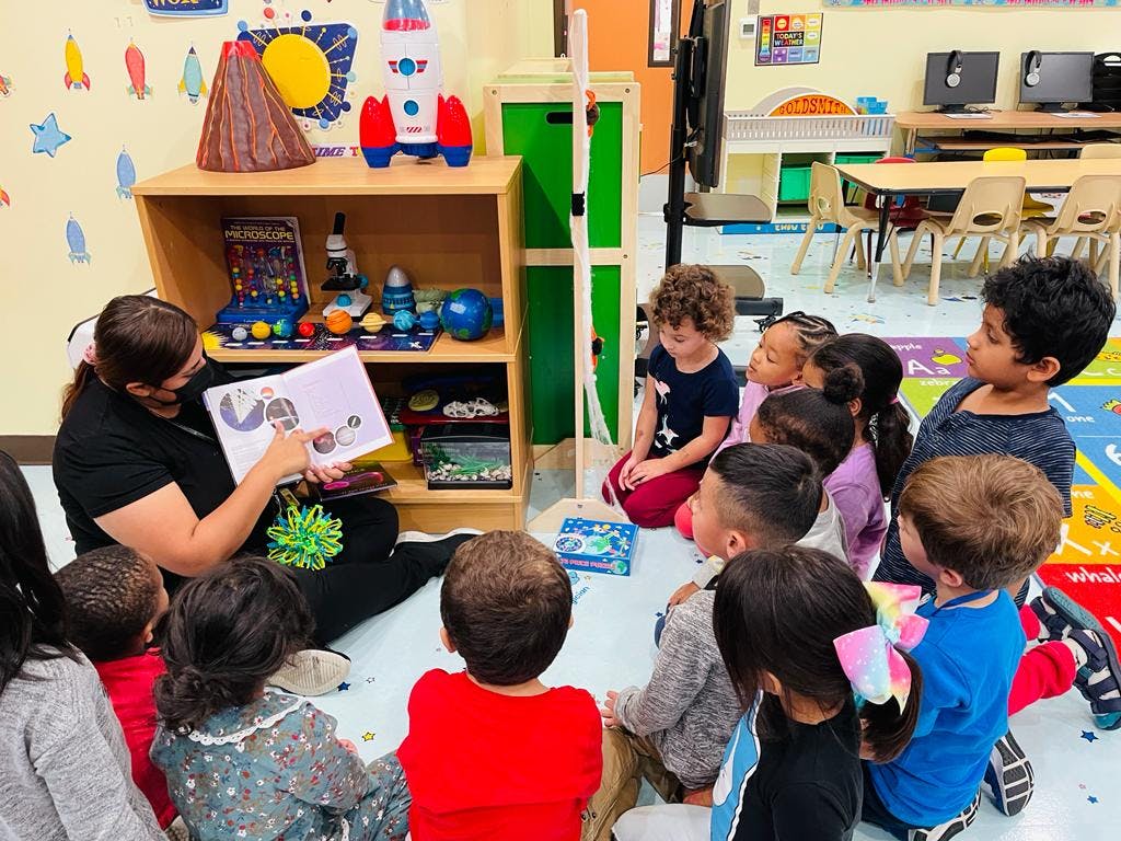 Adult wearing a face mask reading a book to a group of children in a classroom